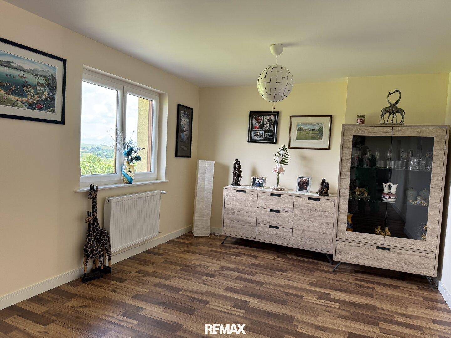Heller Wohnbereich mit Laminatboden, Sideboard und dekorativen Elementen unter einem Deckenlicht.