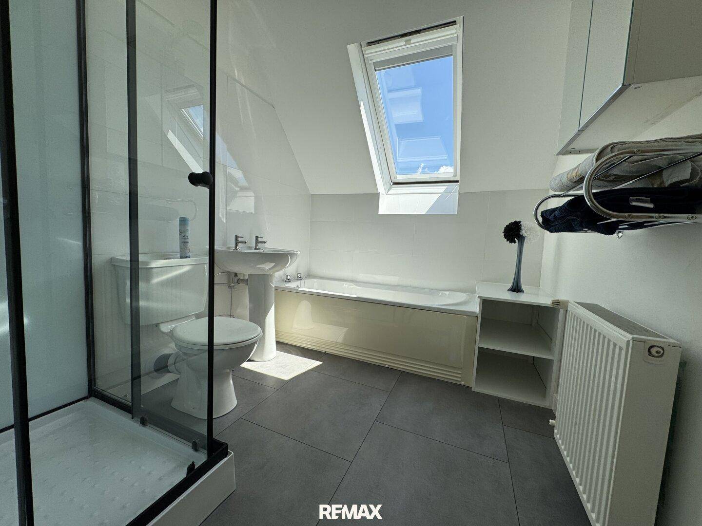 Modernes Badezimmer mit Dusche, Badewanne und Dachfenster, das viel Tageslicht spendet.