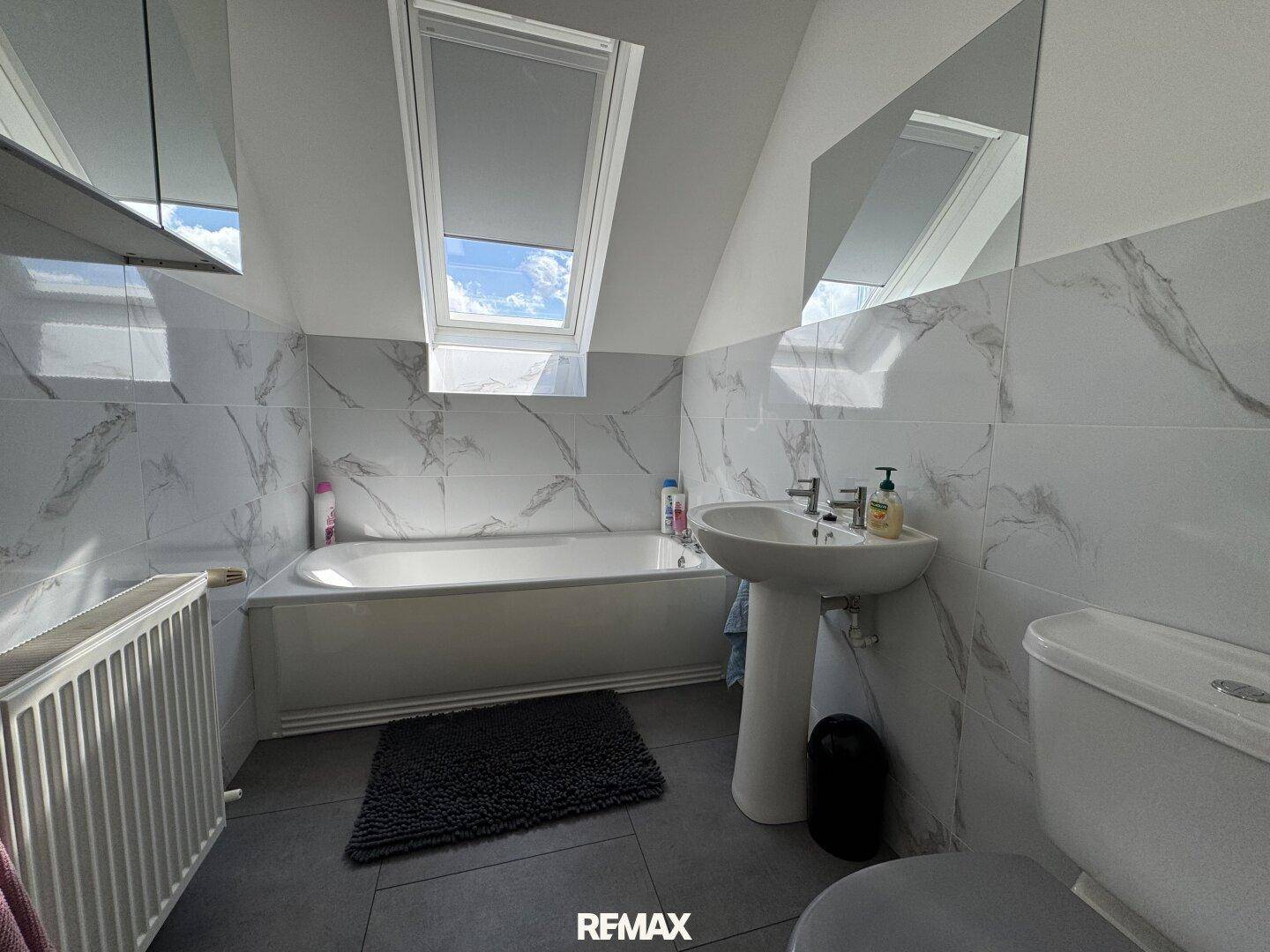 Helles Badezimmer mit Badewanne, Waschbecken und Dachfenster, das den Raum mit Licht füllt.