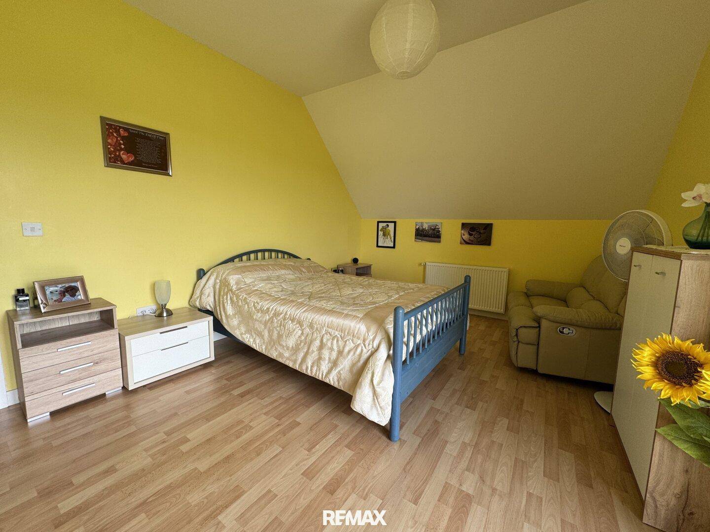 Geräumiges Schlafzimmer mit gelben Wänden, Laminatboden und einem großen Bett.
