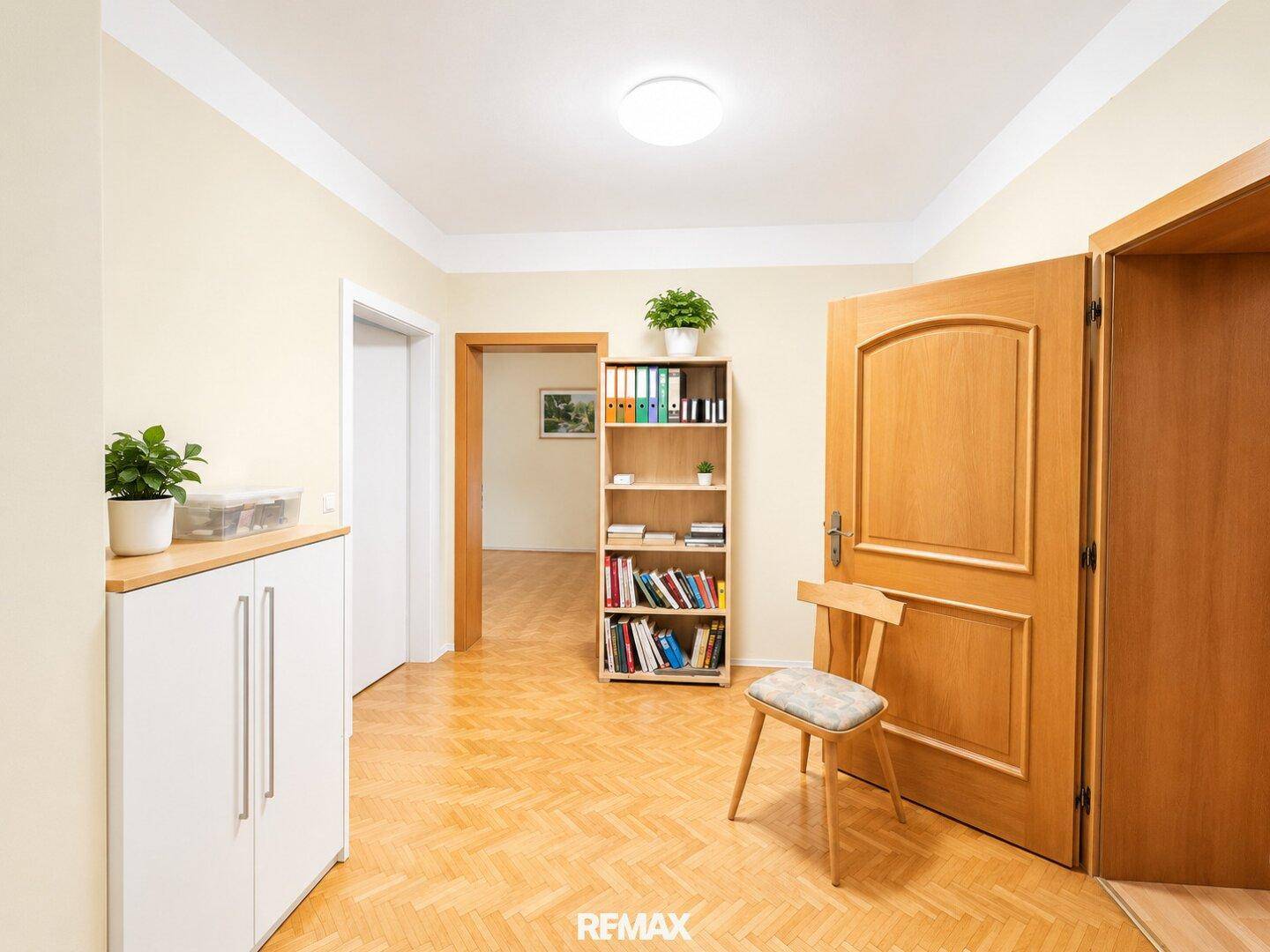 Heller Flur mit Parkettboden, Bücherregal und Schuhschrank, der zu weiteren Räumen führt.