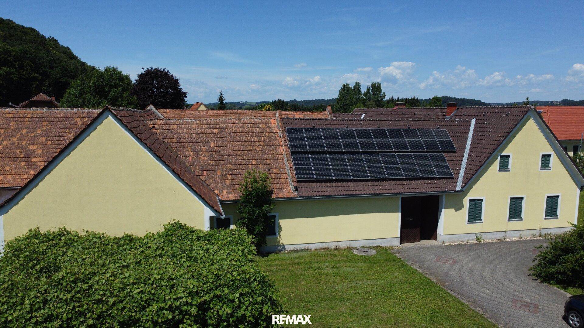 Seitenansicht des Gebäudes mit gelber Fassade, grünen Fensterläden und Solaranlage auf dem Dach.