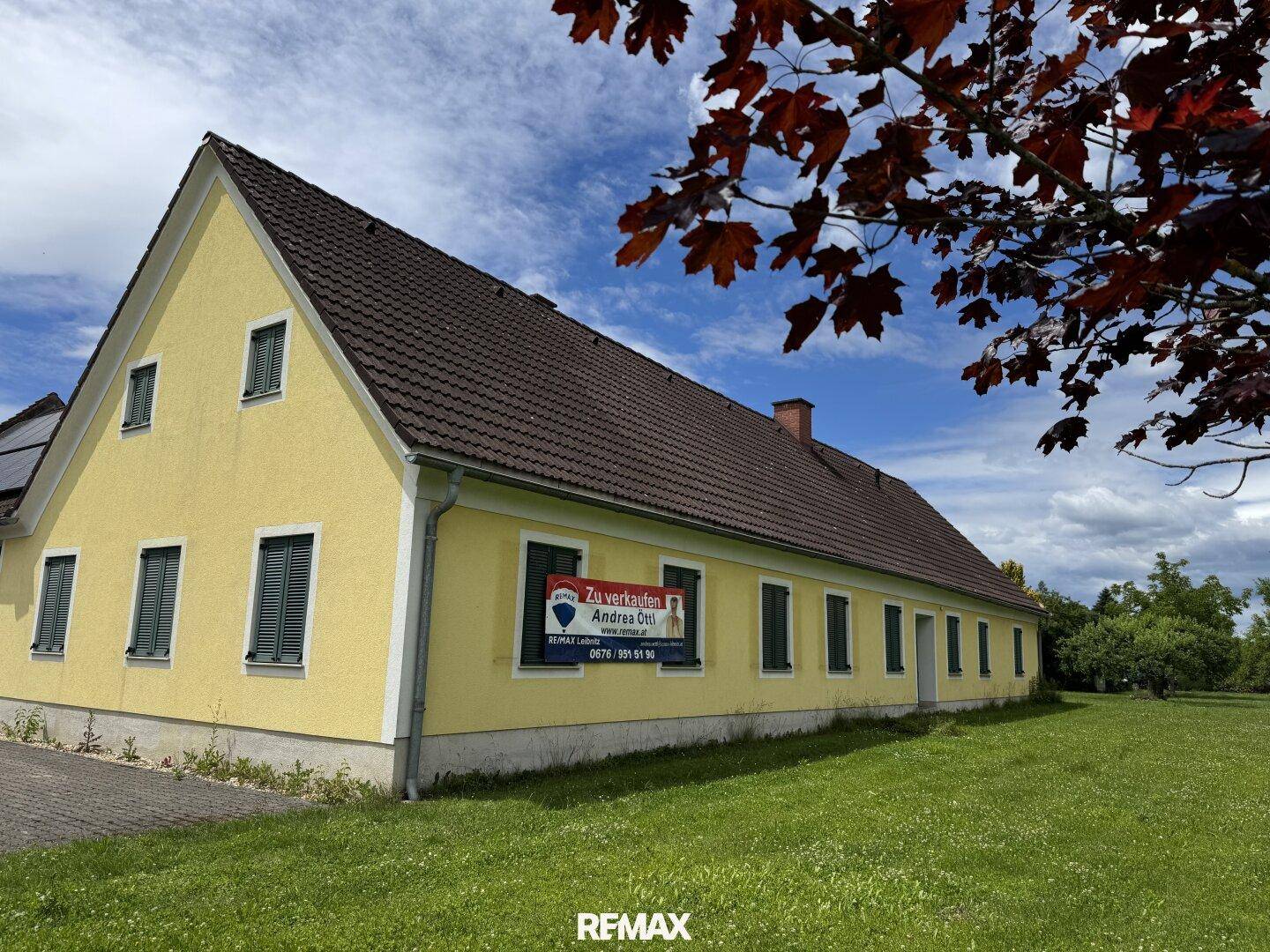 Gelb gestrichenes Gebäude mit braunem Ziegeldach und einem "Zu verkaufen"-Schild auf der Fassade.