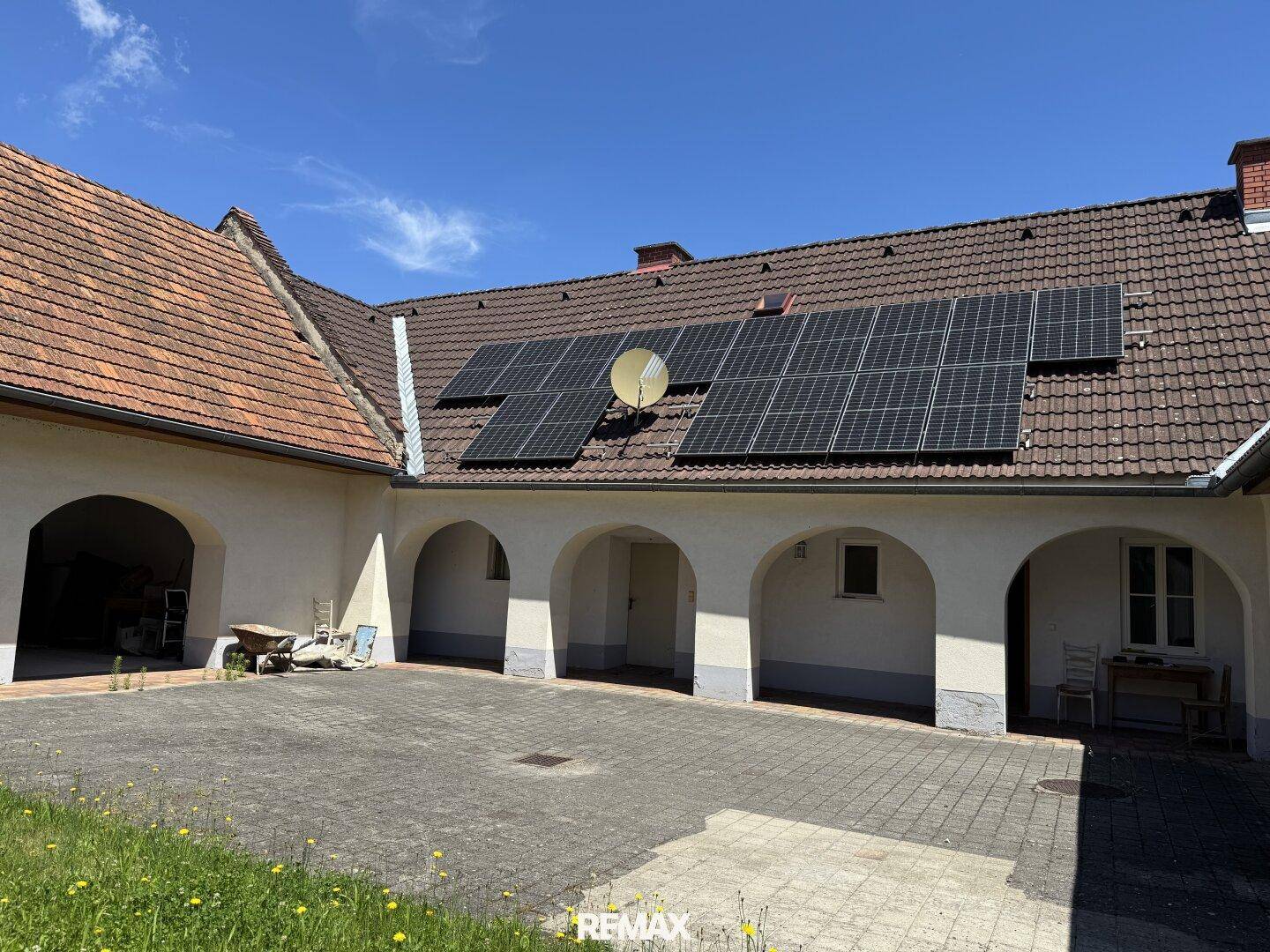 Innenhof mit gepflastertem Bereich, Arkaden und Solaranlage auf dem Ziegeldach des Gebäudes.