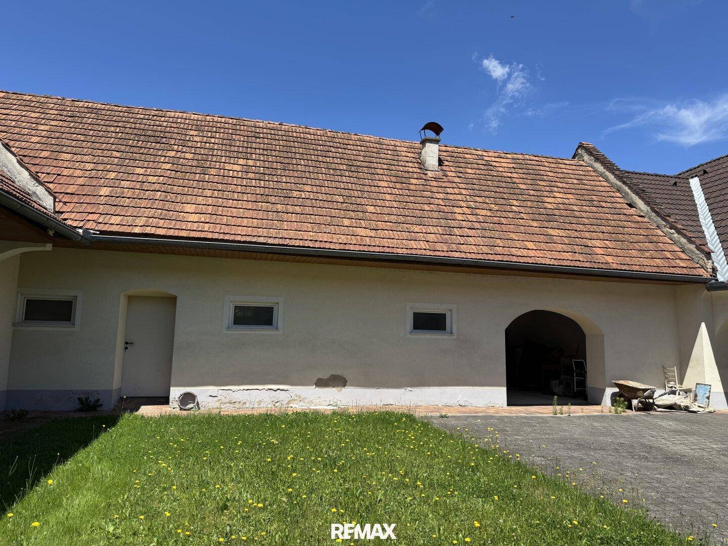 Blick über den Rasen im Innenhof auf einen Gebäudeteil mit Tür, Fenstern und großem Torbogen.