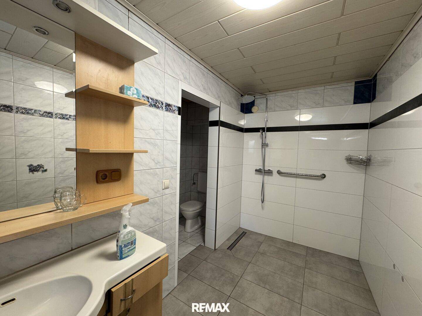 Modern gefliestes Badezimmer mit ebenerdiger Dusche, Haltegriffen und Einzelwaschbecken.