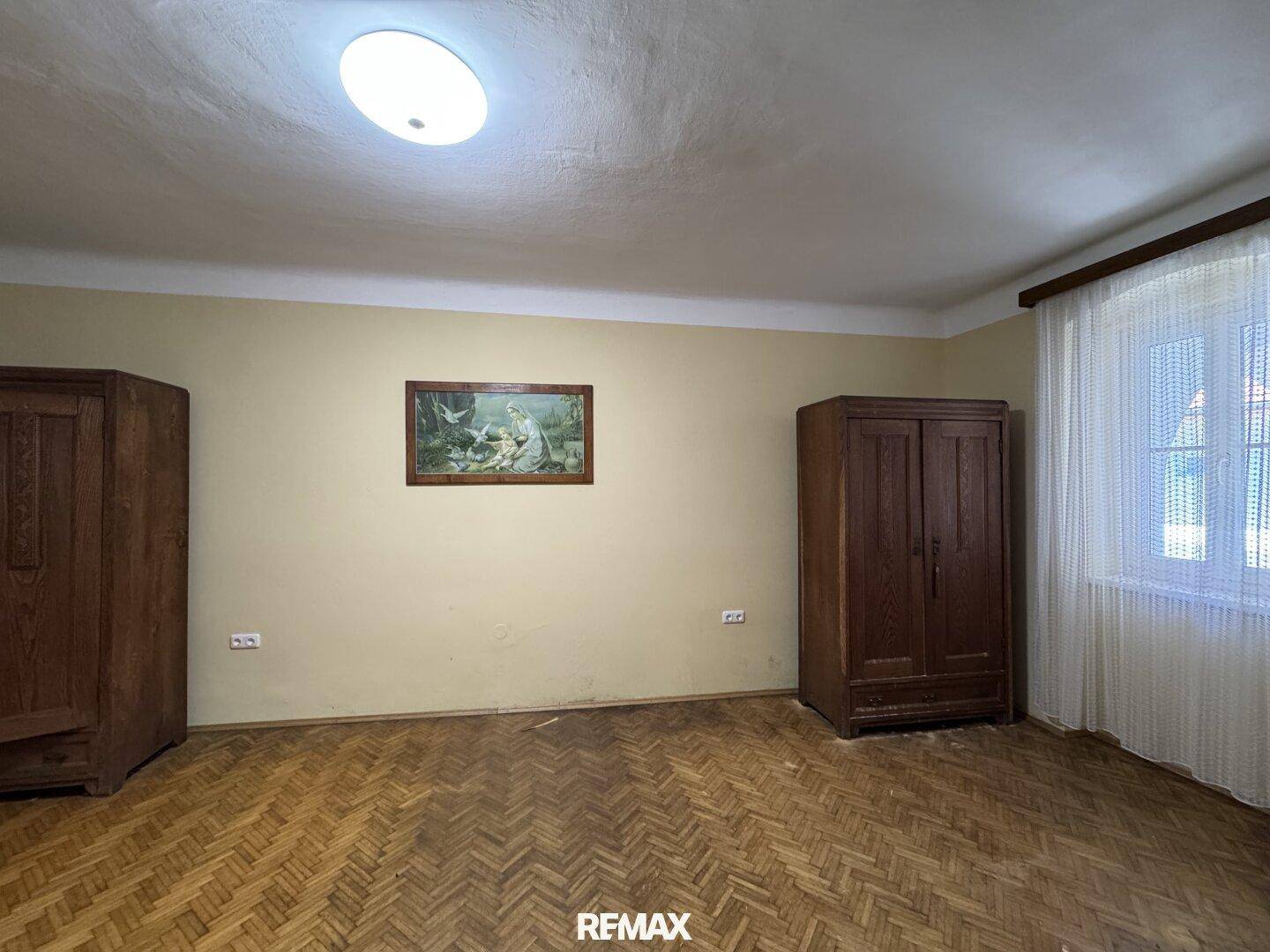 Geräumiges Zimmer mit Fischgrätparkett, gelben Wänden und traditionellen Holzschränken.