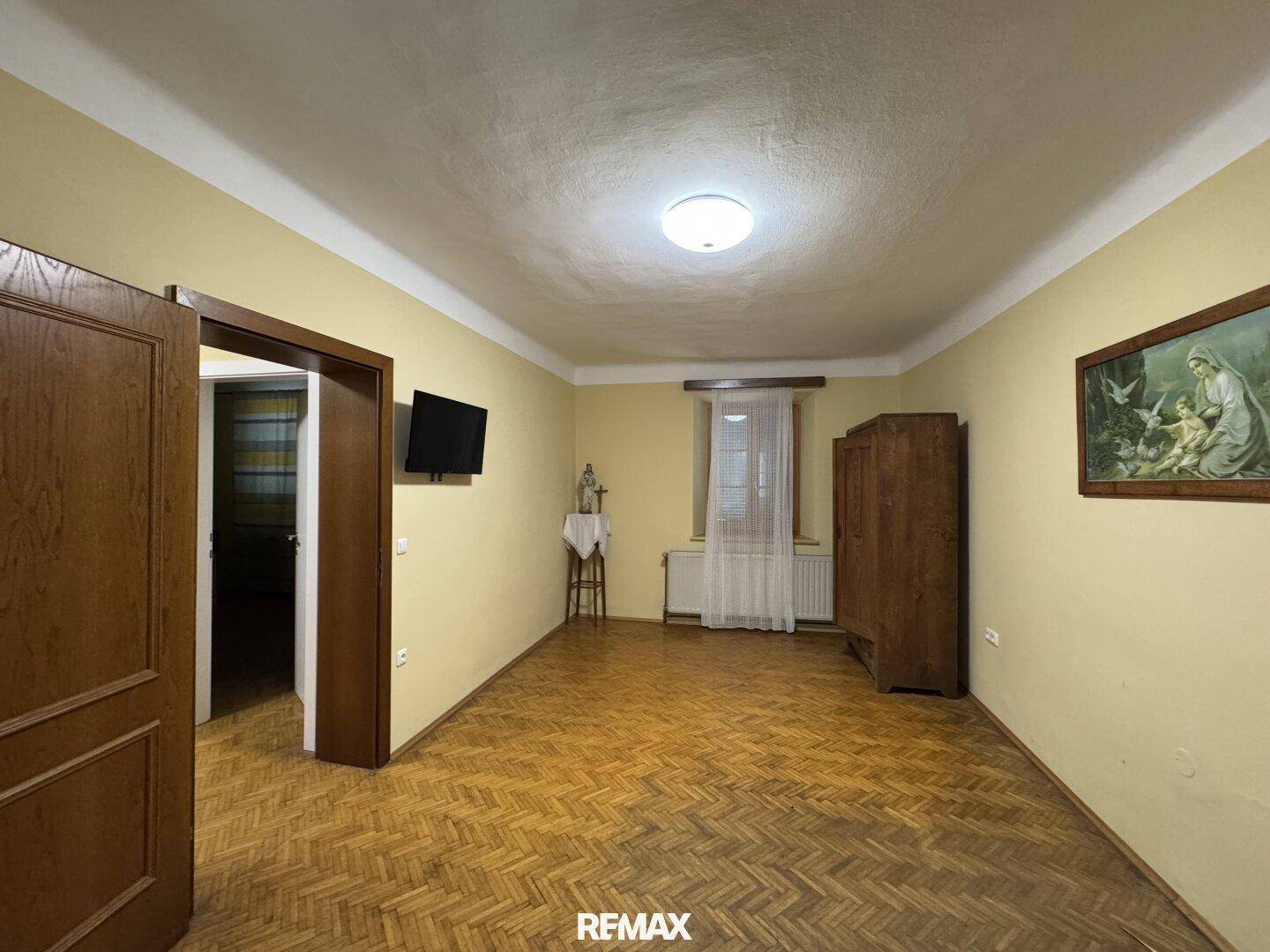 Großes Zimmer mit Fischgrätparkett, gelben Wänden und Zugang zu einem weiteren Raum.