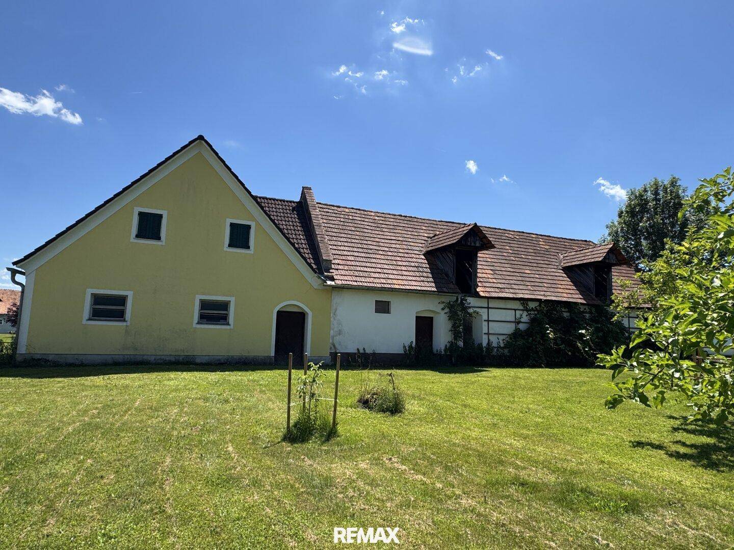 Seitenansicht des Gebäudes mit weißer Fassade, Gaubenfenstern und umgebender grüner Landschaft.