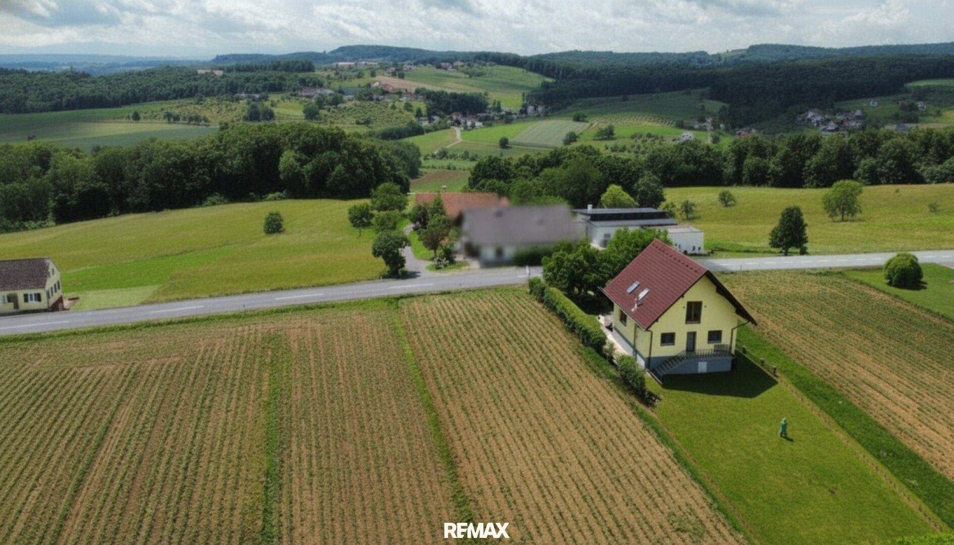 Weitläufige Luftaufnahme eines gelben Hauses in ländlicher Umgebung mit Feldern und Hügeln im Hintergrund.