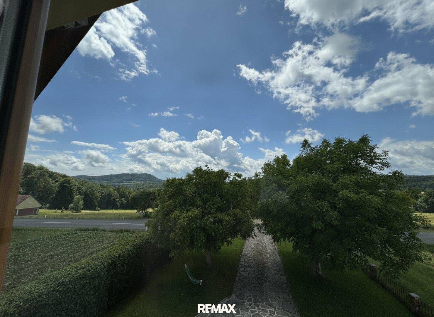 Weitläufiger Blick aus dem Fenster auf die grüne Landschaft mit Bäumen und einem blauen Himmel.