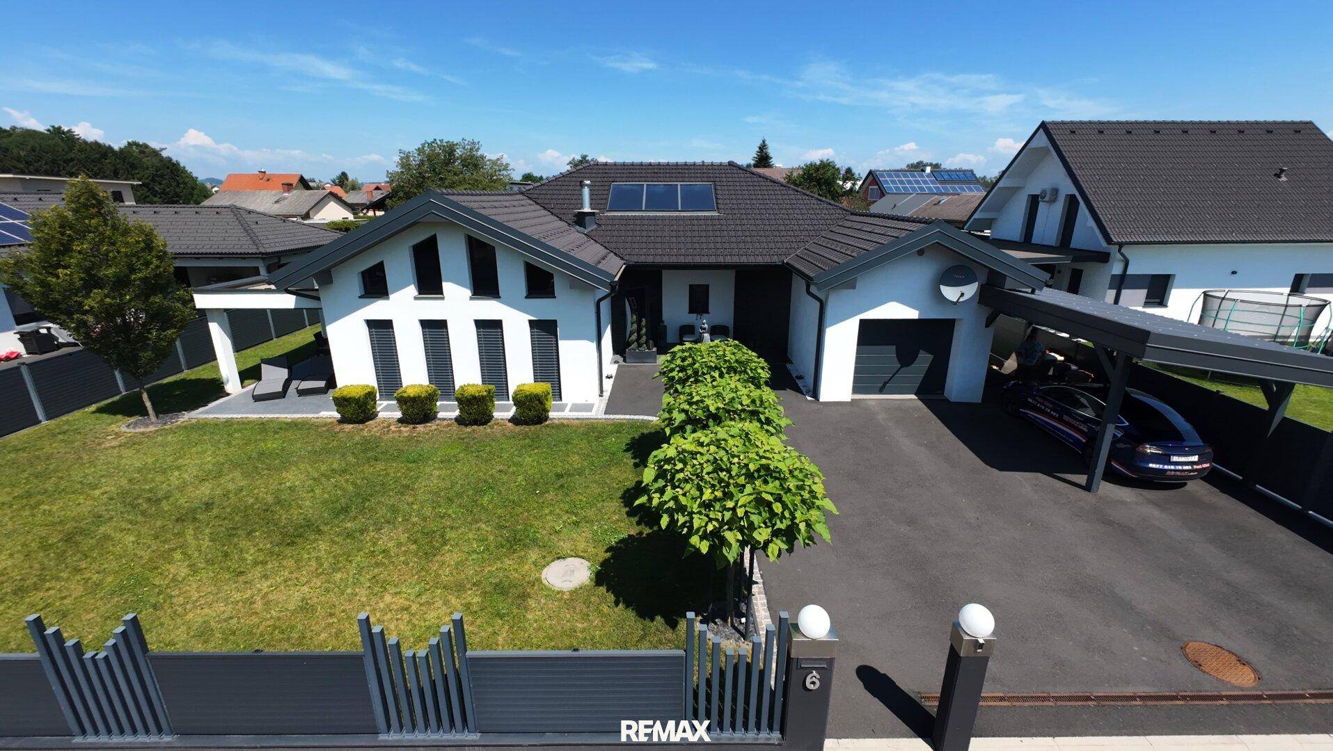 Luftaufnahme des modernen Einfamilienhauses mit Carport, gepflegtem Vorgarten und Solarpaneelen auf dem Dach.
