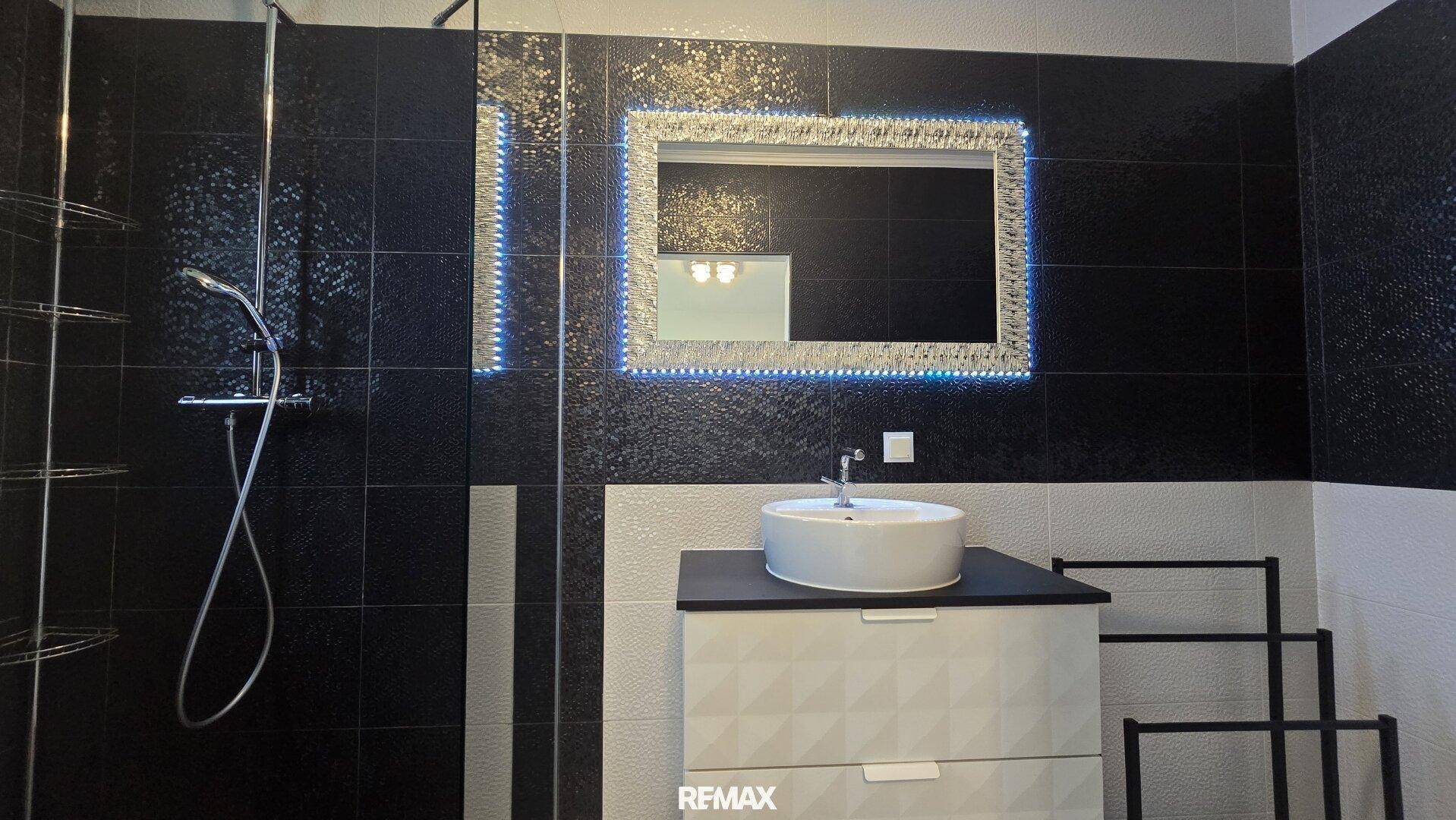 Modernes Badezimmer mit begehbarer Dusche, beleuchtetem Spiegel und stilvollen Fliesen.