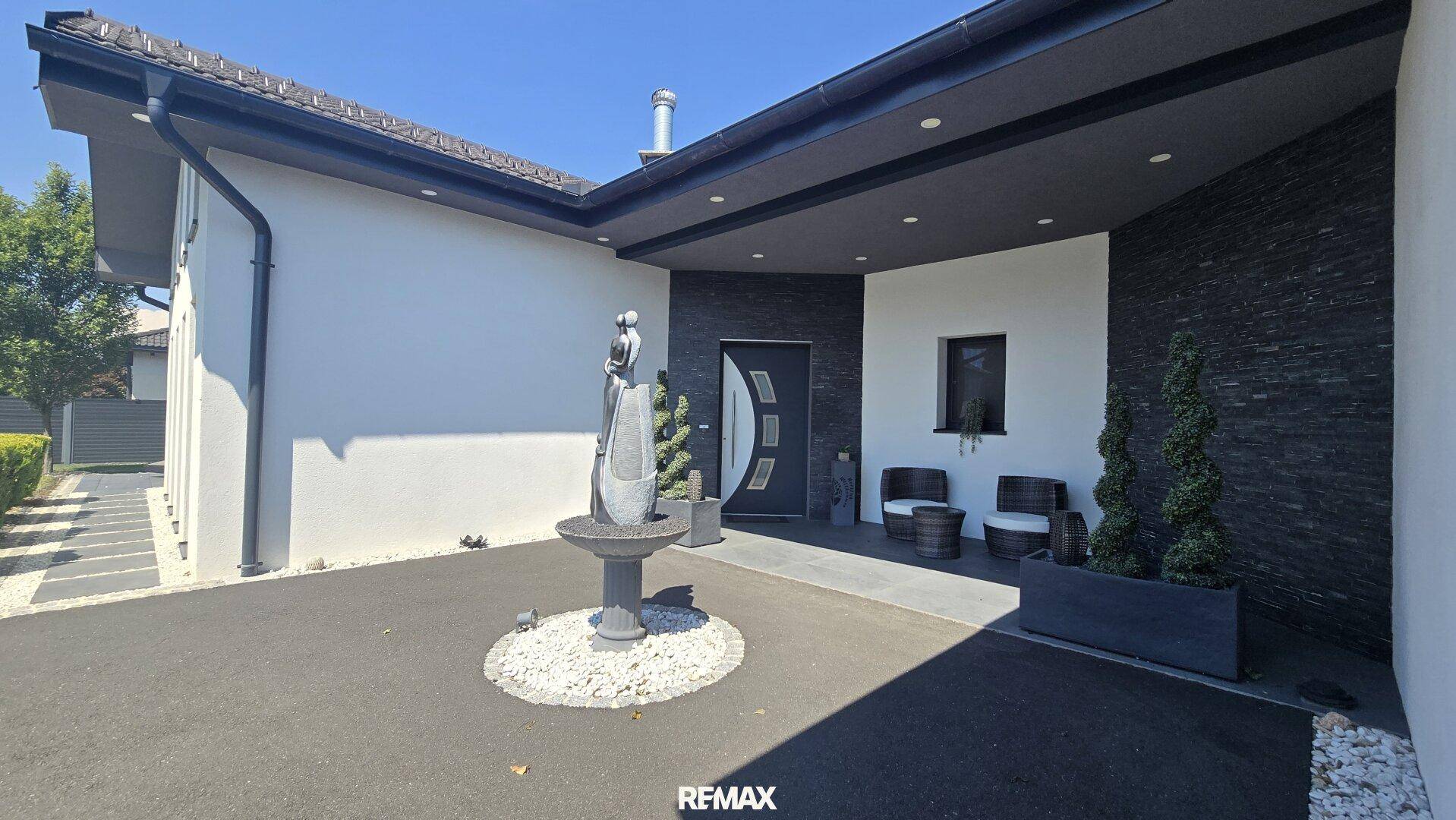Moderner Eingangsbereich des Hauses mit dunkler Steinverkleidung, Zierbrunnen und Sitzgelegenheiten.
