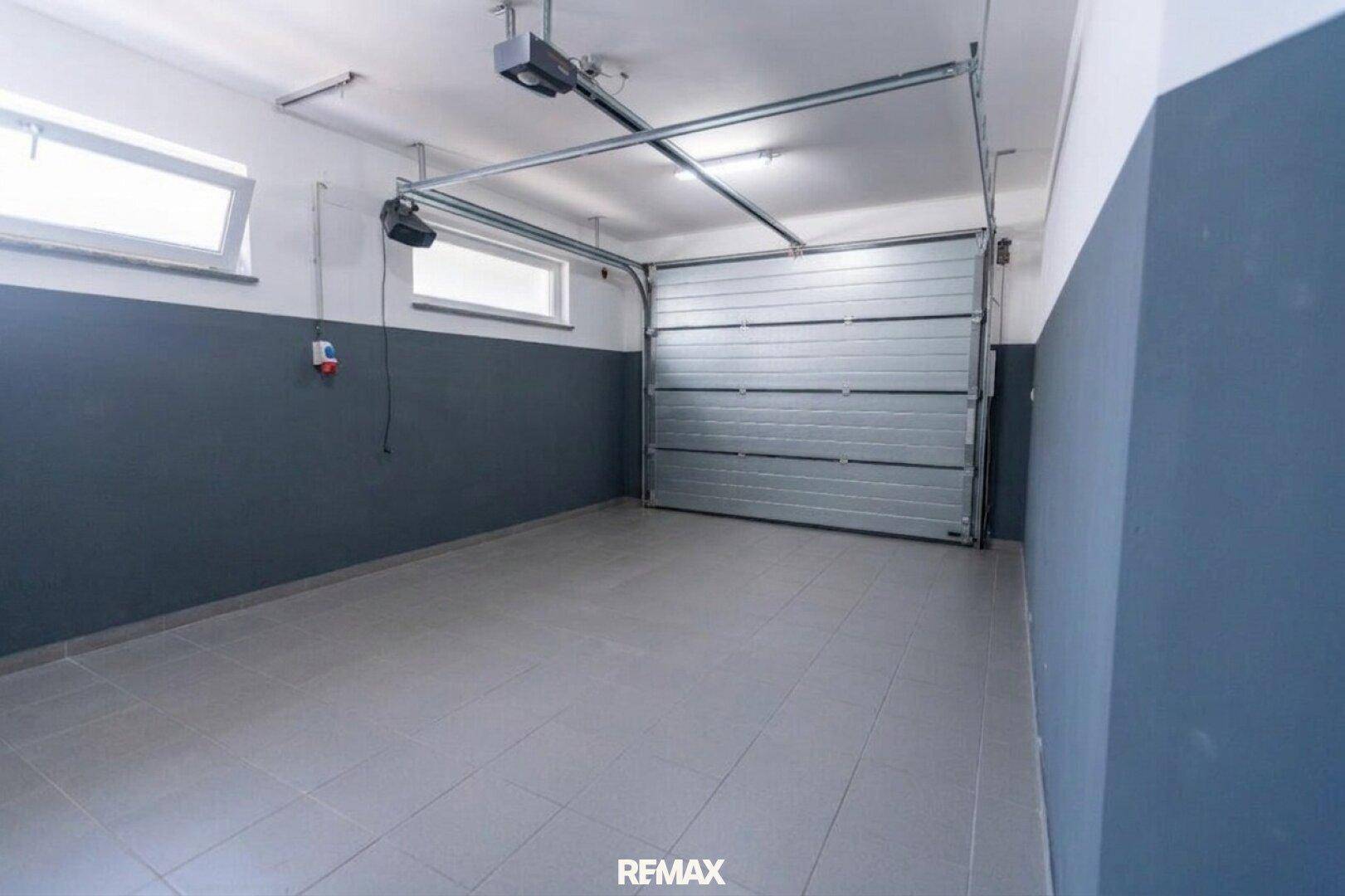 Geräumige Garage mit automatischem Garagentor, Fliesenboden und Fenstern für Tageslicht.