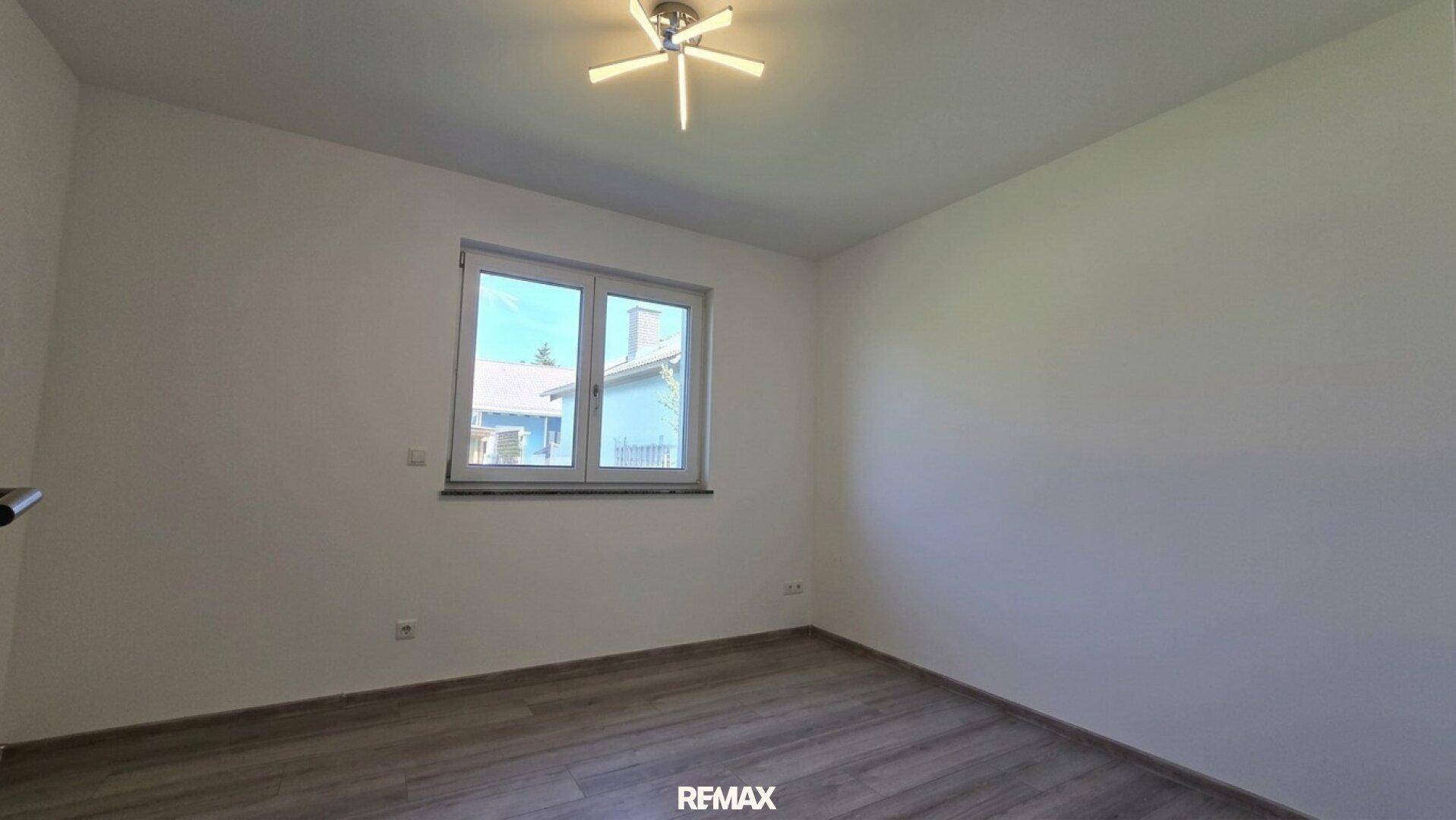 Helles Schlafzimmer mit modernem Laminatboden und Fenster mit Blick ins Grüne.
