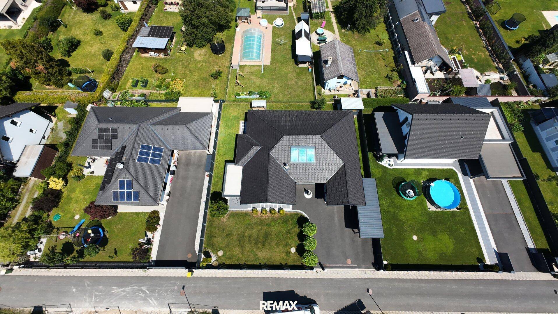 Luftaufnahme eines Wohngebiets mit mehreren modernen Häusern, Gärten, Pools und Solaranlagen auf den Dächern.