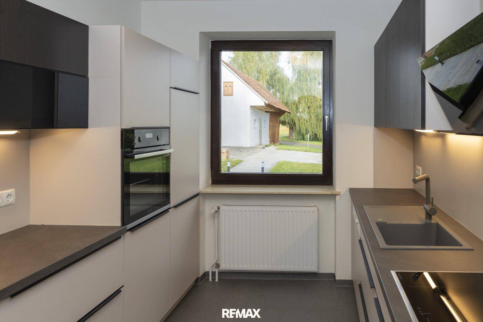 Moderne Küche mit integriertem Backofen, Spüle und Fenster mit Blick ins Grüne.