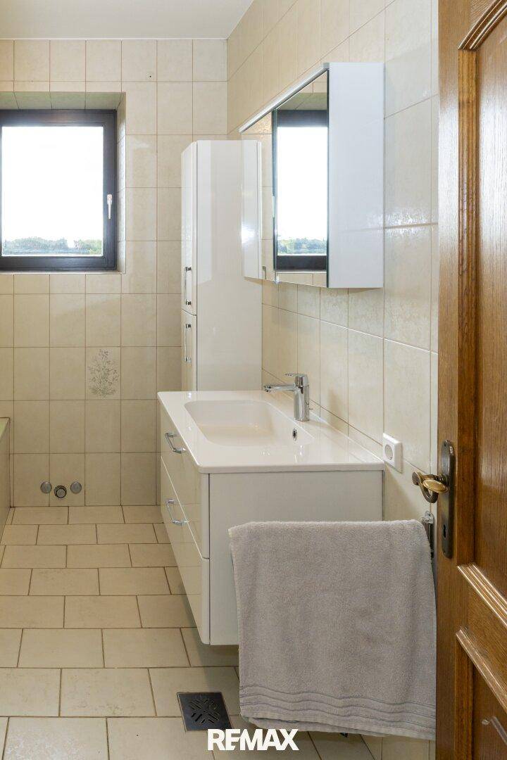 Helles Badezimmer mit beigen Fliesen, modernem Waschtisch und Spiegelschrank.