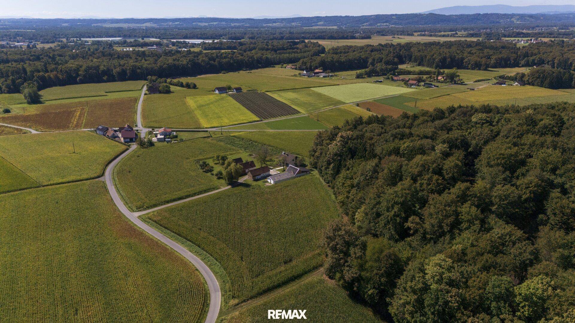 Weitläufige Luftaufnahme des Anwesens mit angrenzenden Feldern und Wäldern unter blauem Himmel.