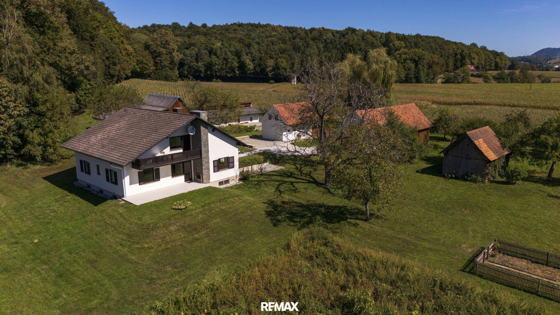 Draufsicht auf das Haupthaus und Nebengebäude, eingebettet in grüne Wiesen und Bäume.