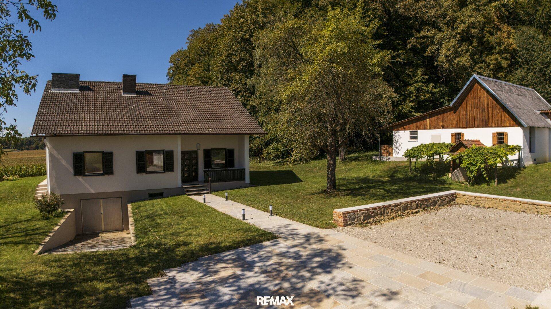 Vorderansicht des Hauses mit gepflastertem Zugang, Kiesfläche und umgebender Natur.