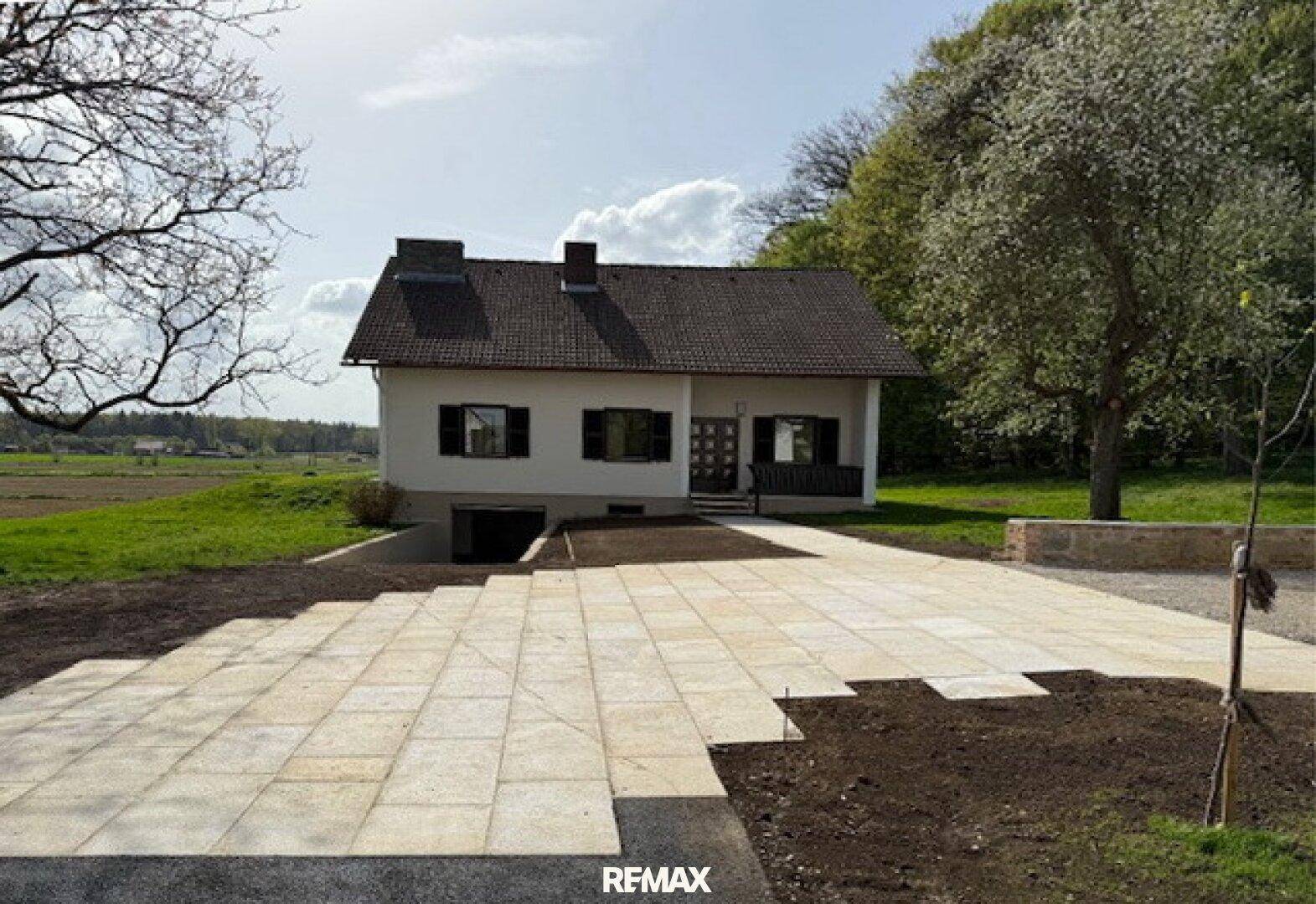 Hausansicht mit neu angelegter gepflasterter Fläche und vorbereitetem Gartenbereich.