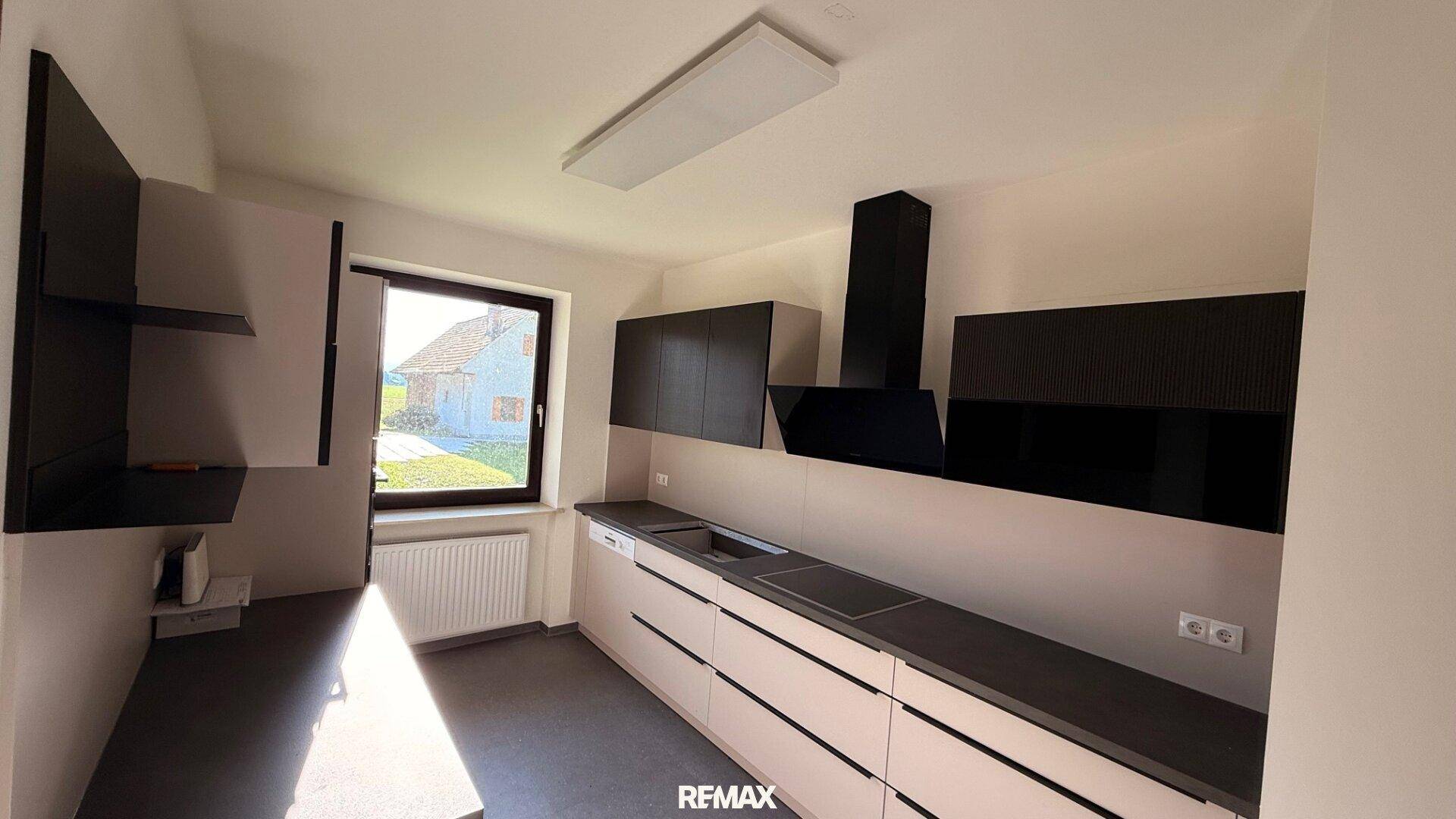 Moderne Küche mit schwarzen und hellgrauen Schränken, integrierten Geräten und Fenster.