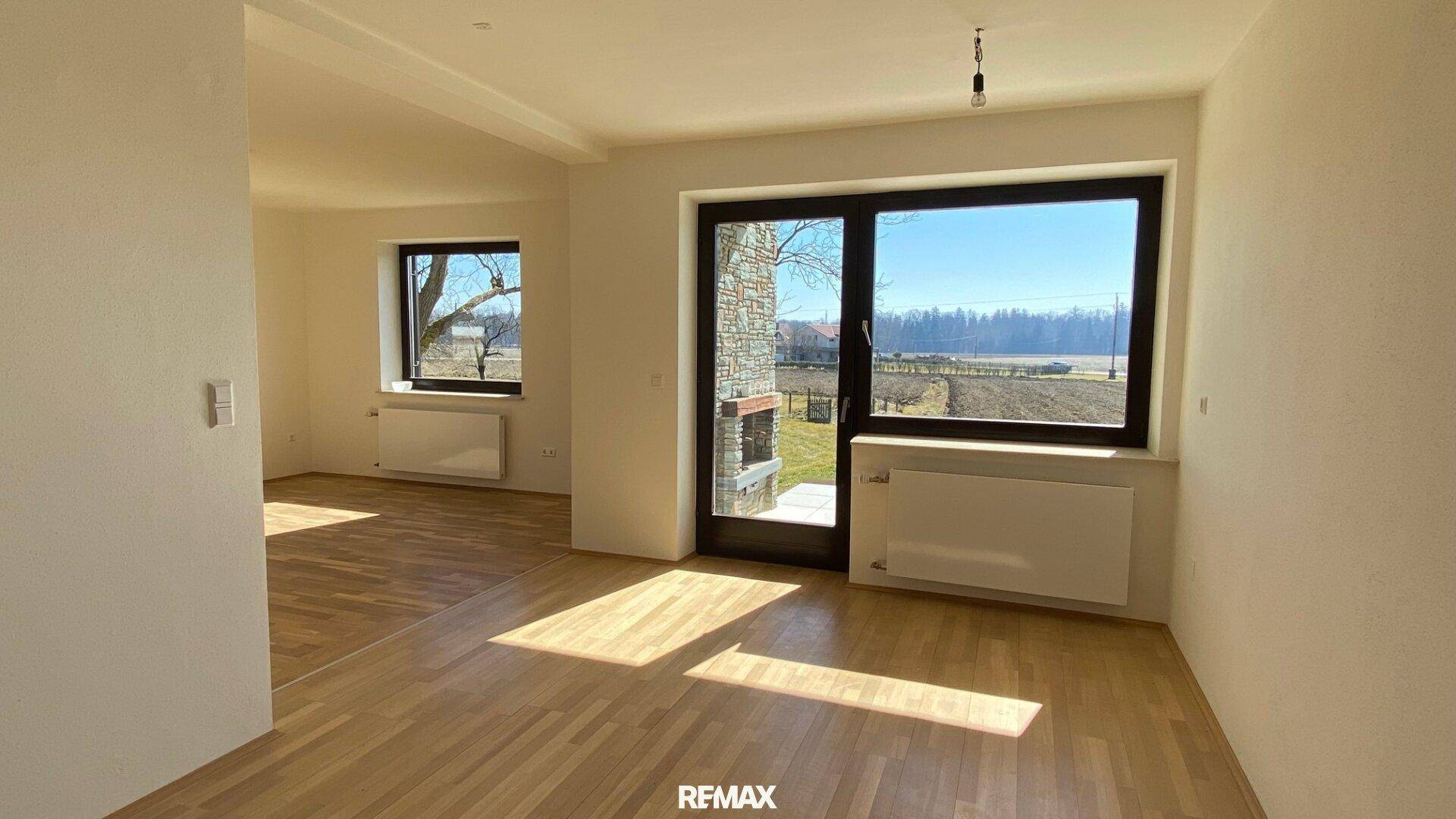 Heller Wohnbereich mit Holzboden, großen Fenstern und Blick auf die umliegende Landschaft.