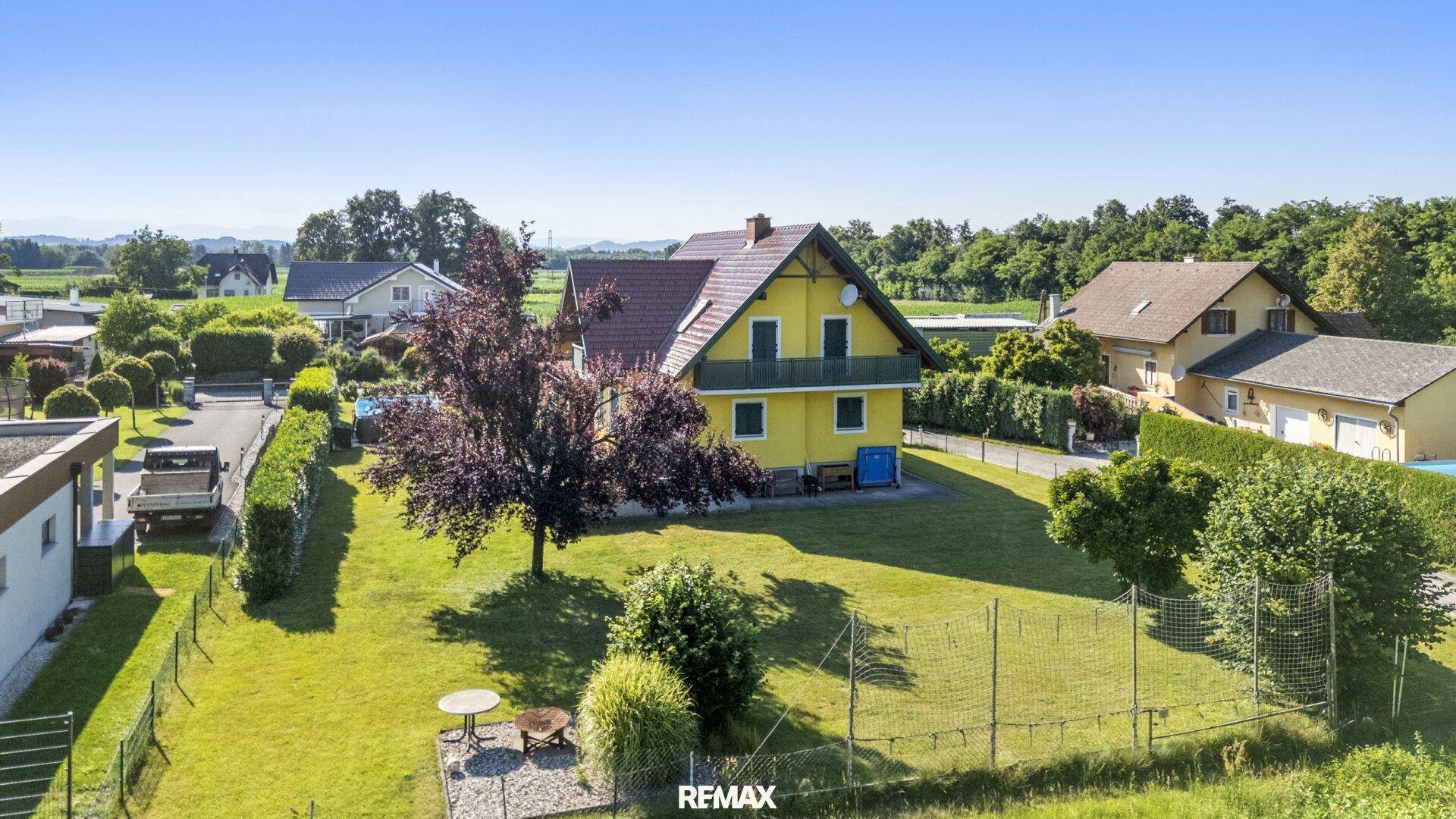 Weitläufiger Gartenbereich mit Rasenfläche und kleiner Sitzecke, umgeben von ländlicher Landschaft.