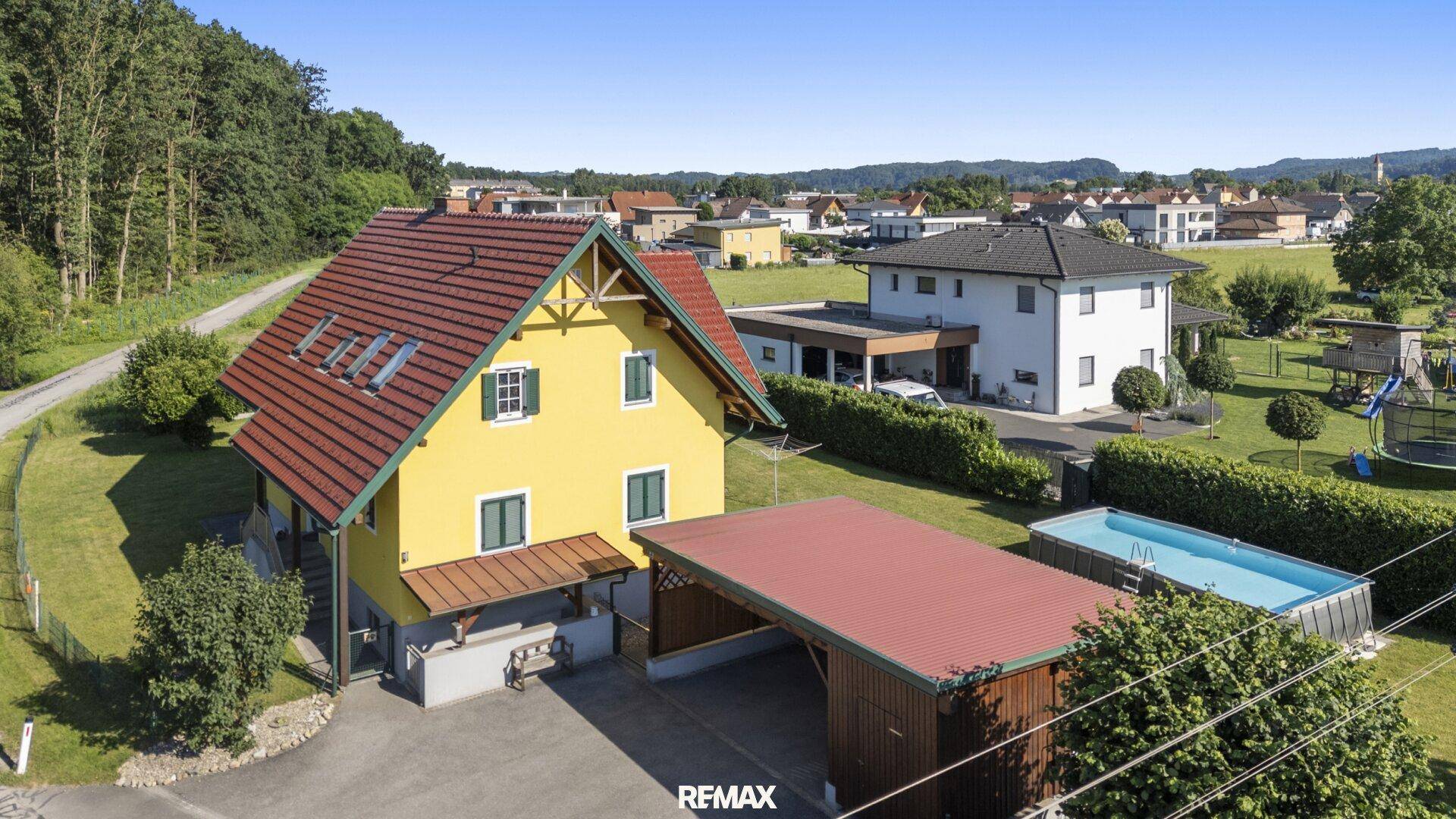 Vorderansicht des Hauses mit Carport, Swimmingpool und Blick auf die umliegende Wohnsiedlung.