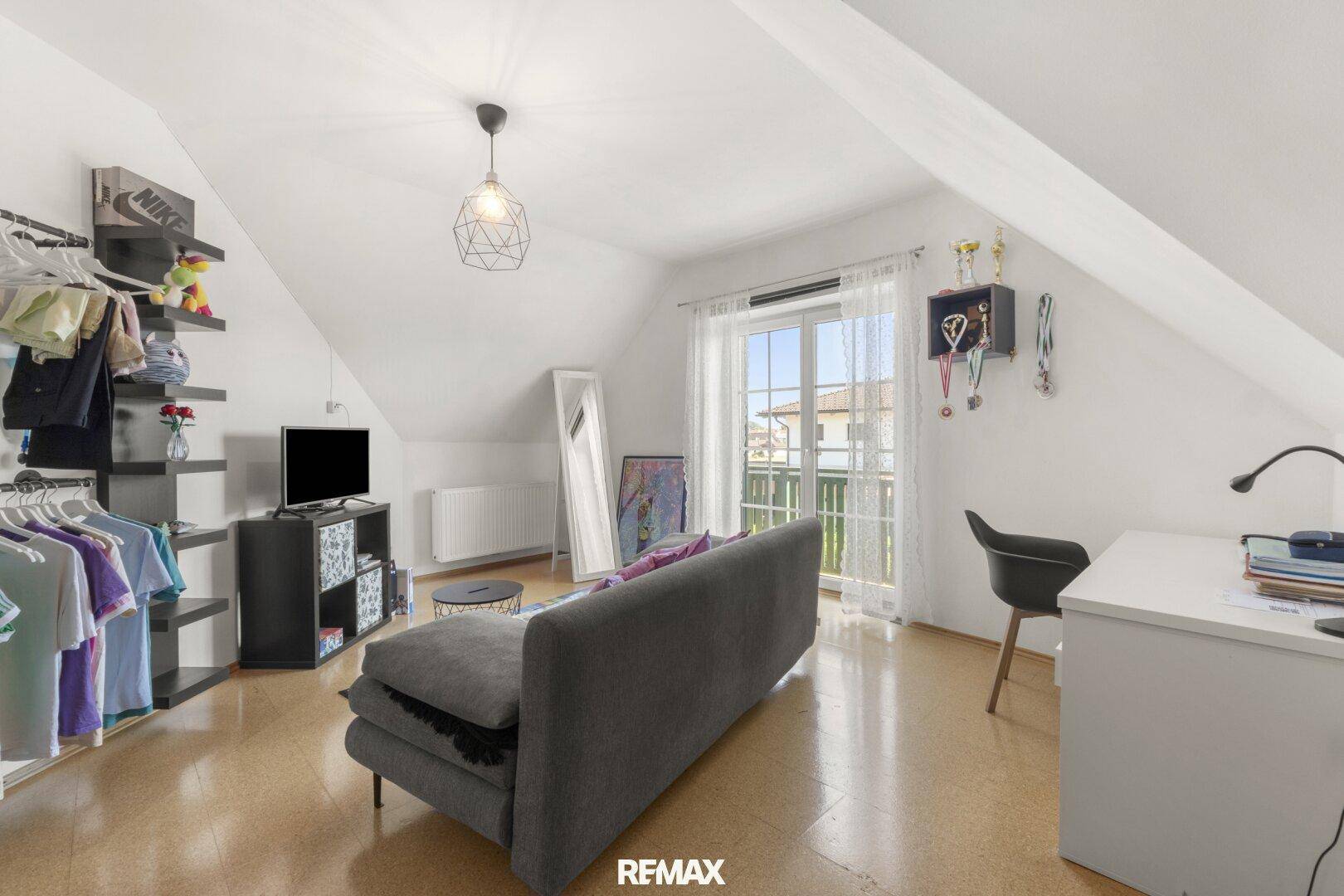 Dachzimmer mit schrägen Wänden, Korkboden und Zugang zu einem Balkon, ideal als Schlaf- oder Wohnbereich.