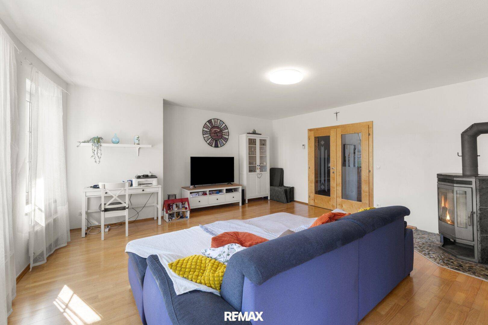 Gemütliches Wohnzimmer mit Kaminofen, Holzboden und Zugang zu weiteren Räumen durch Holztüren.