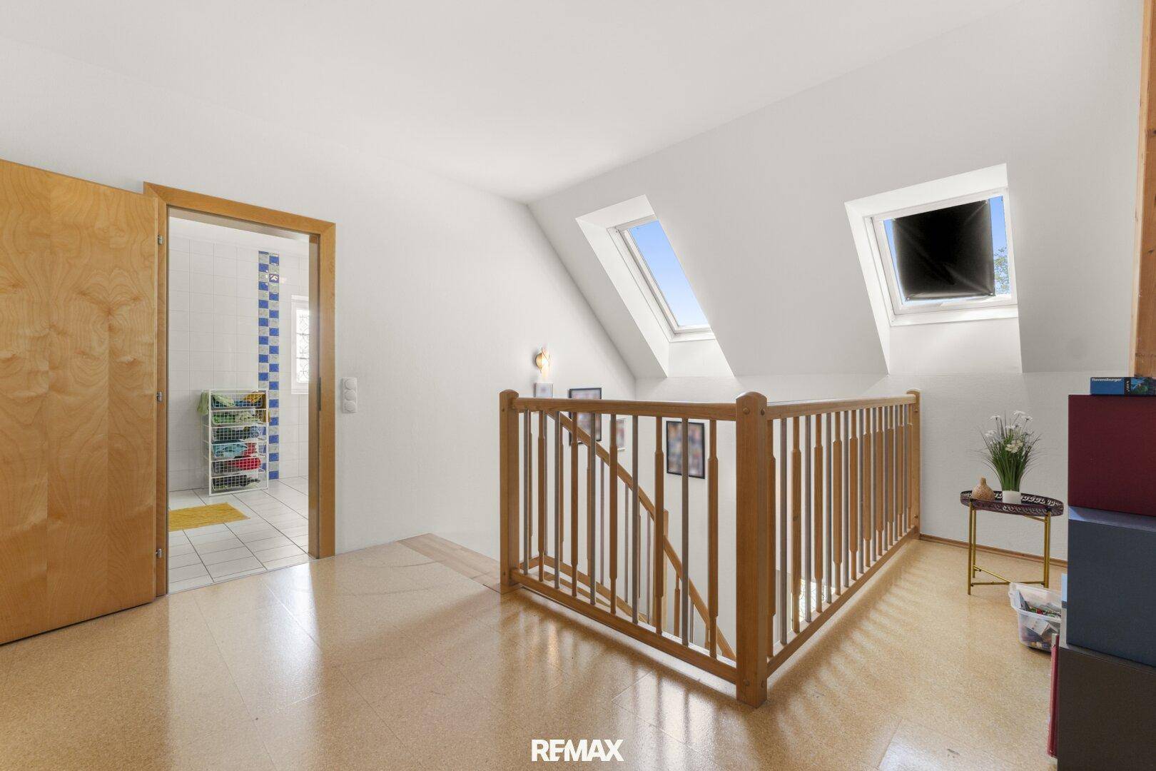 Heller Flur im Obergeschoss mit Holzgeländer, Korkboden und Dachfenstern für natürliches Licht.