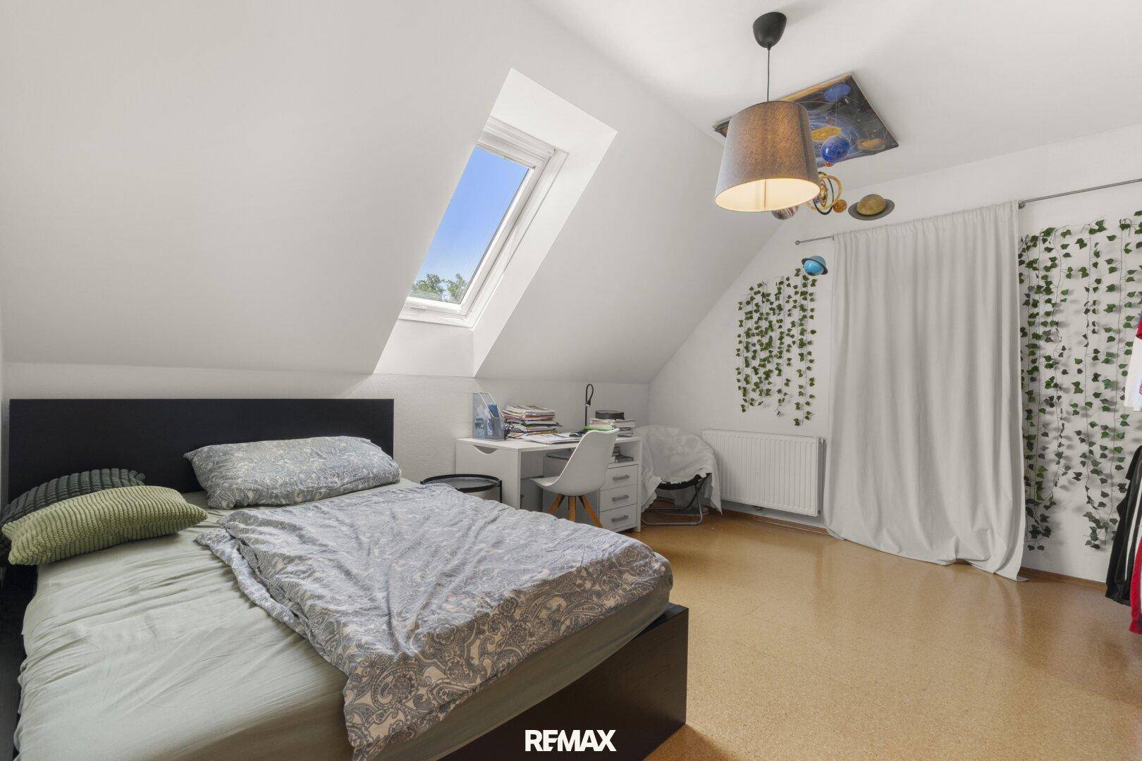 Gemütliches Schlafzimmer im Dachgeschoss mit Bett, schräger Decke, Dachfenster und Korkboden.