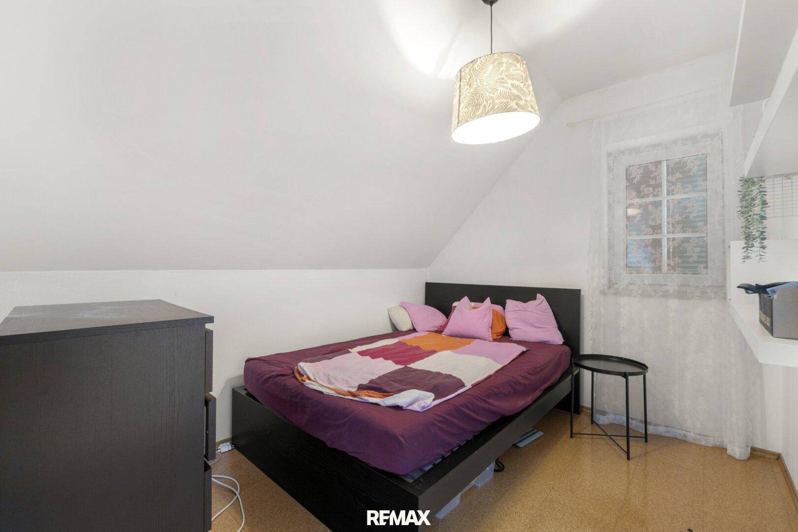 Schlafzimmer im Dachgeschoss mit Bett, schräger Decke, Fenster und Korkboden.