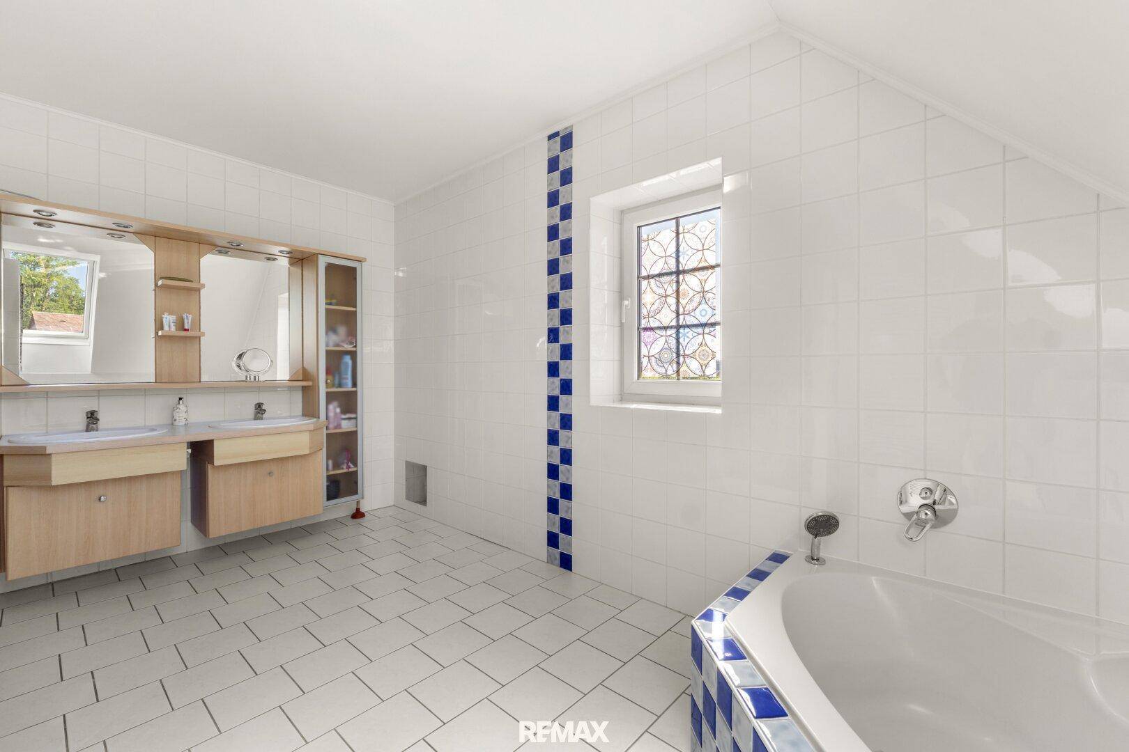 Geräumiges Badezimmer im Dachgeschoss mit weißen Fliesen, Doppelwaschbecken und Eckbadewanne.