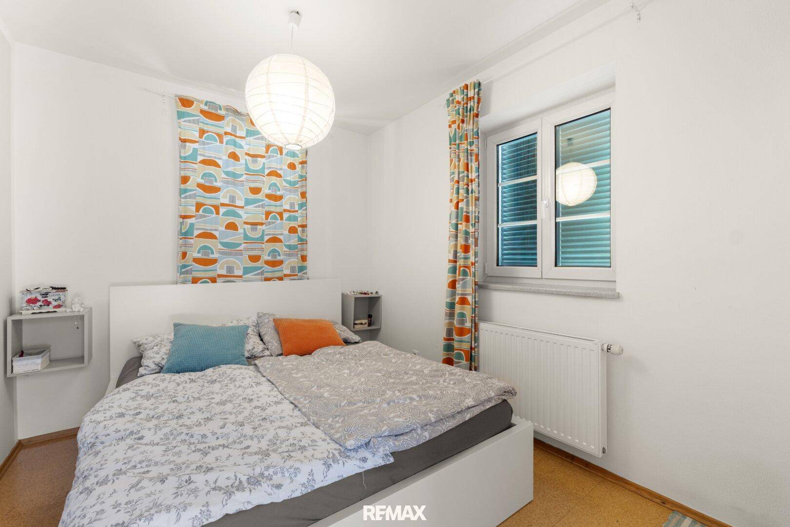 Schlafzimmer mit Doppelbett, hellem Fenster und farbenfrohen Vorhängen, die für Akzente sorgen.