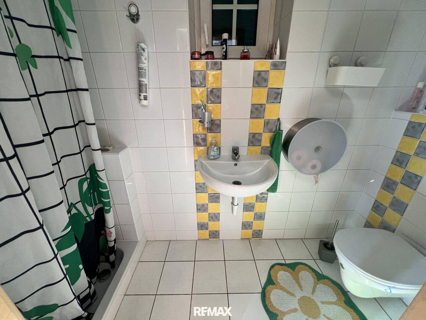 Badezimmer mit weiß-gelb karierten Fliesen, Waschbecken, Toilette und Duschbereich mit Vorhang.