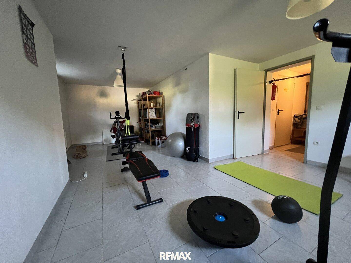 Geräumiger Fitnessraum im Keller mit Fliesenboden und verschiedenen Trainingsgeräten.
