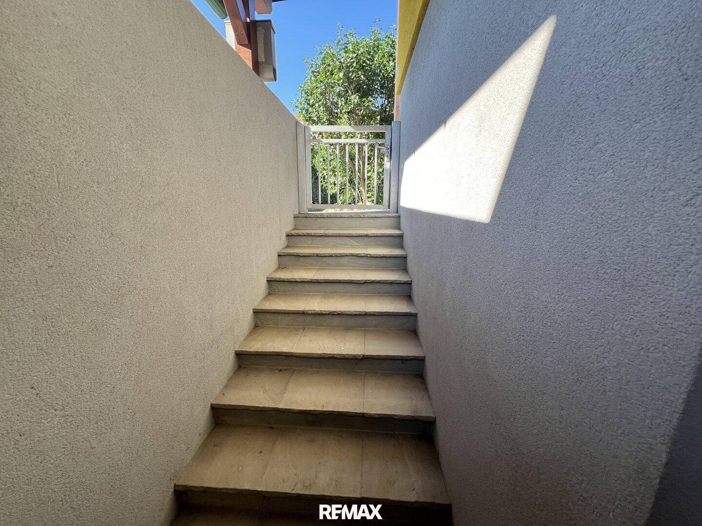 Steintreppe führt hinunter zu einem Eingangsbereich, umgeben von verputzten Wänden.