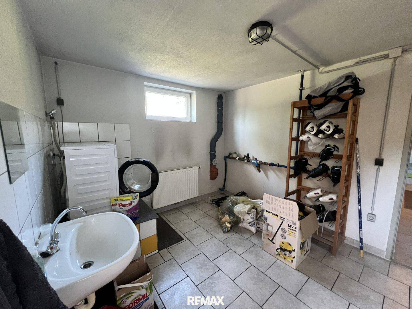 Funktionale Waschküche mit Waschmaschine, Waschbecken und Regal für Schuhe im Untergeschoss.