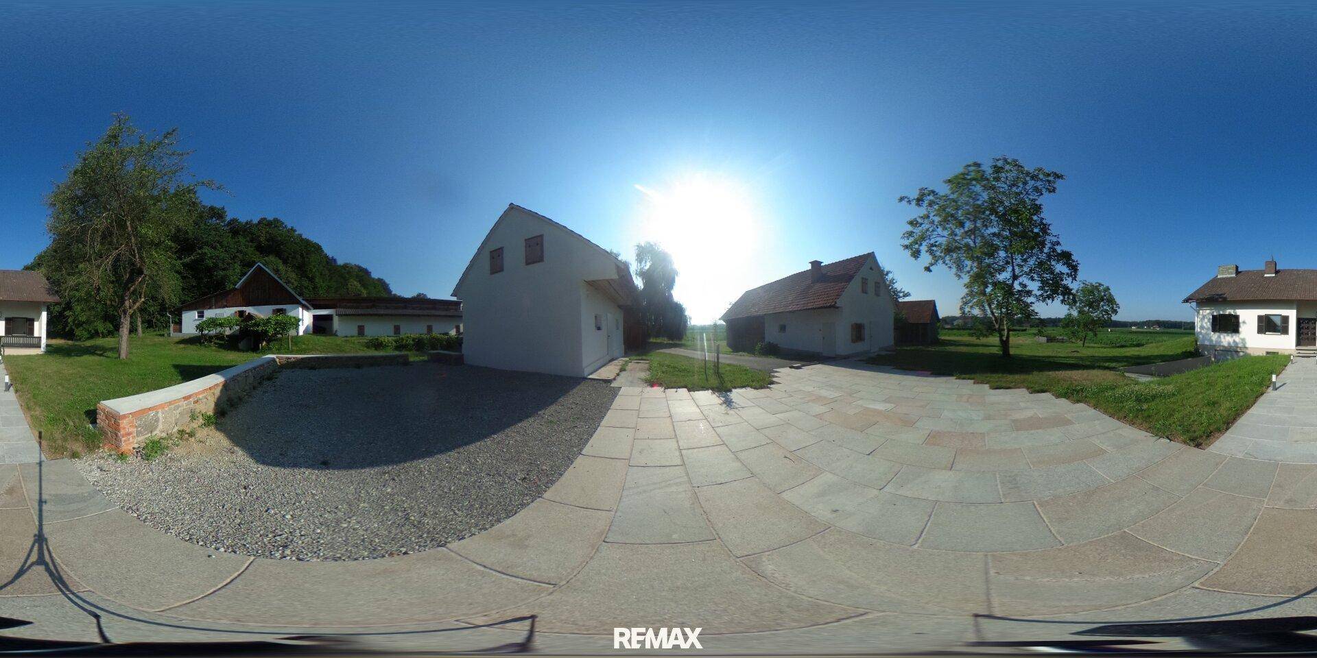 Panoramablick auf das Anwesen mit Haupthaus, Nebengebäuden und gepflastertem Vorplatz unter strahlender Sonne.