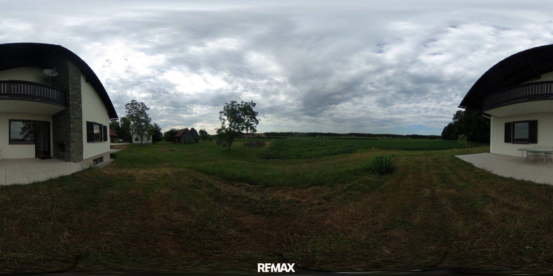 Zwei moderne Gebäude mit Balkonen und weitem Blick über grüne Felder unter bewölktem Himmel.