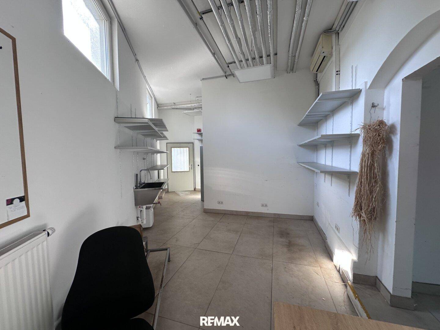 Nutzraum mit Regalen, Spülbecken und sichtbaren Rohren an der Decke.