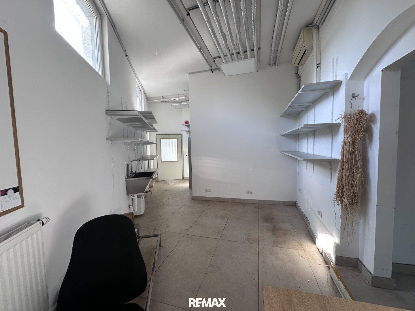 Nutzraum mit Regalen, Spülbecken und sichtbaren Rohren an der Decke.