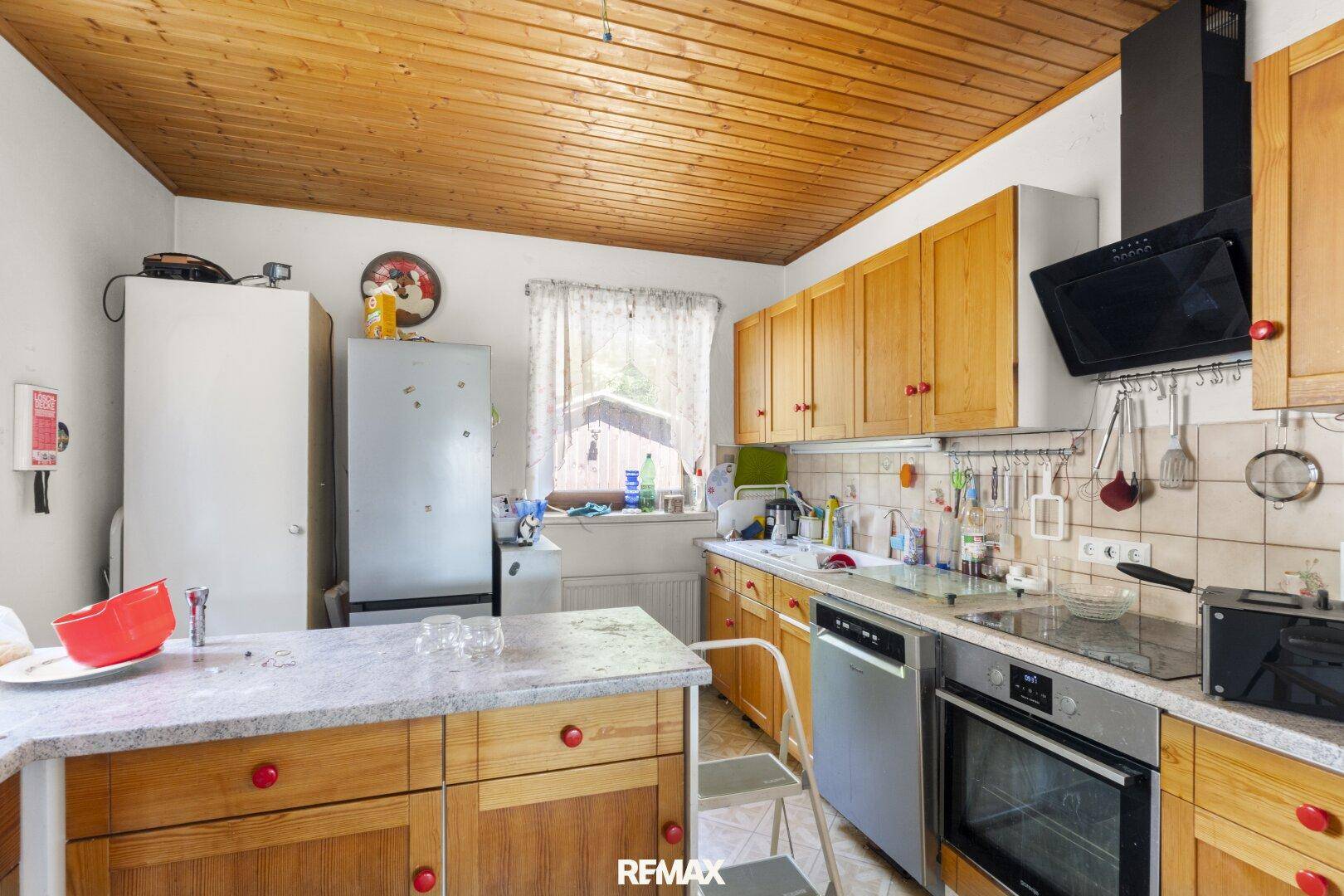 Küche mit Holzschränken, Fliesenrückwand und modernen Geräten, ergänzt durch eine Holzdecke.