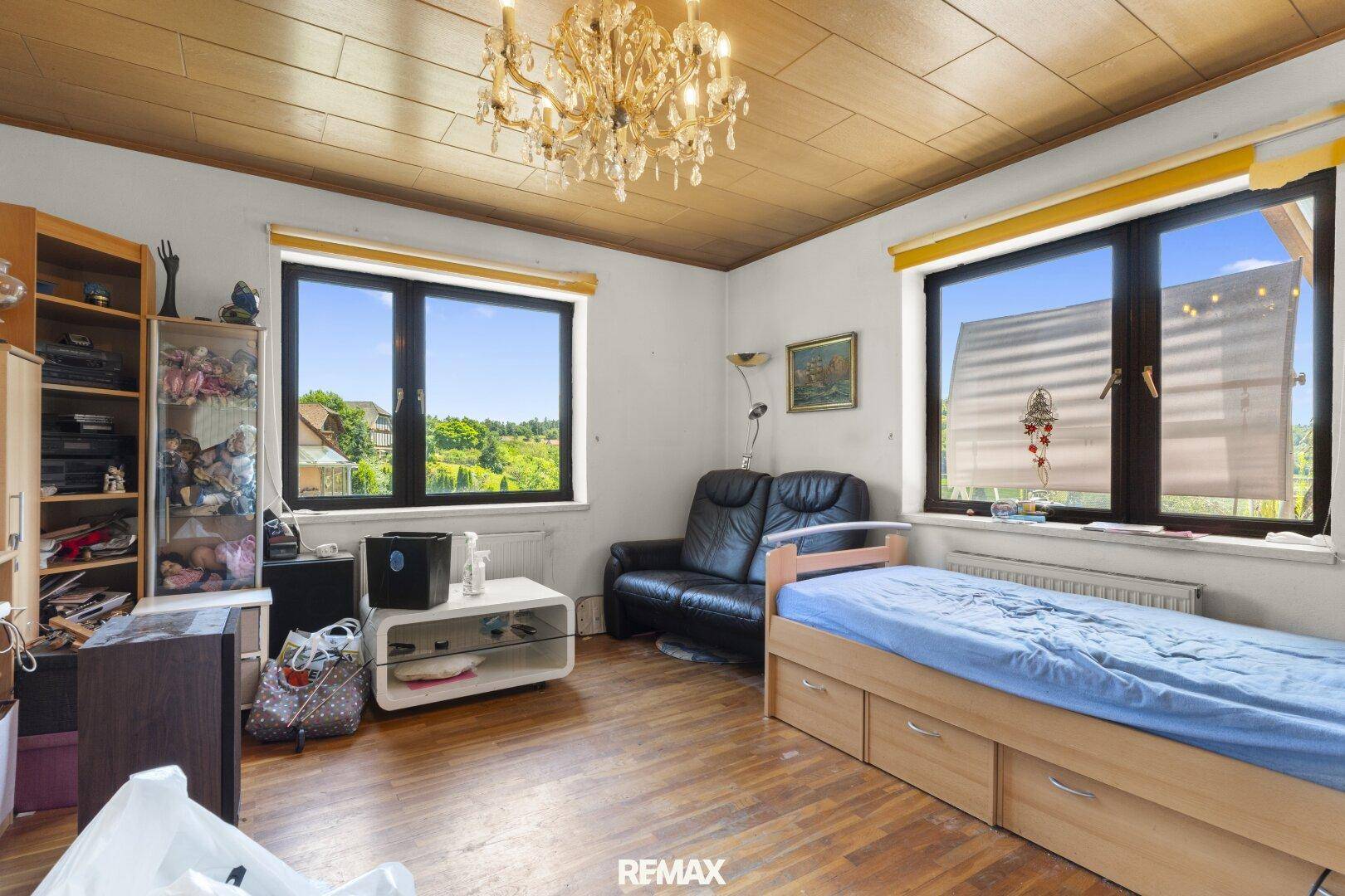 Schlafzimmer mit Holzboden, Holzdecke und zwei Fenstern, die einen angenehmen Blick ins Grüne bieten.