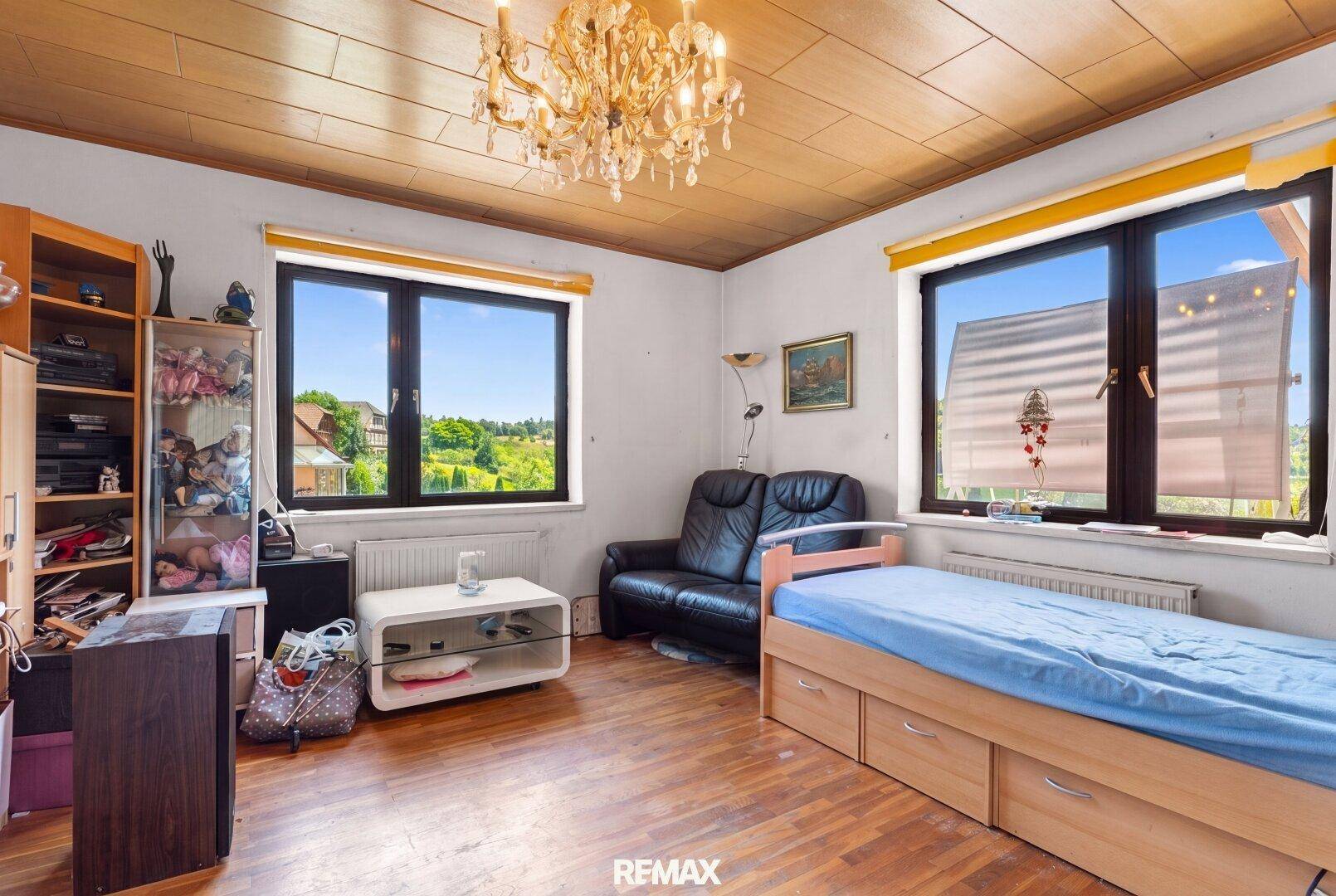 Helles Schlafzimmer mit Holzboden, Holzdecke und großen Fenstern, die viel Tageslicht hereinlassen.