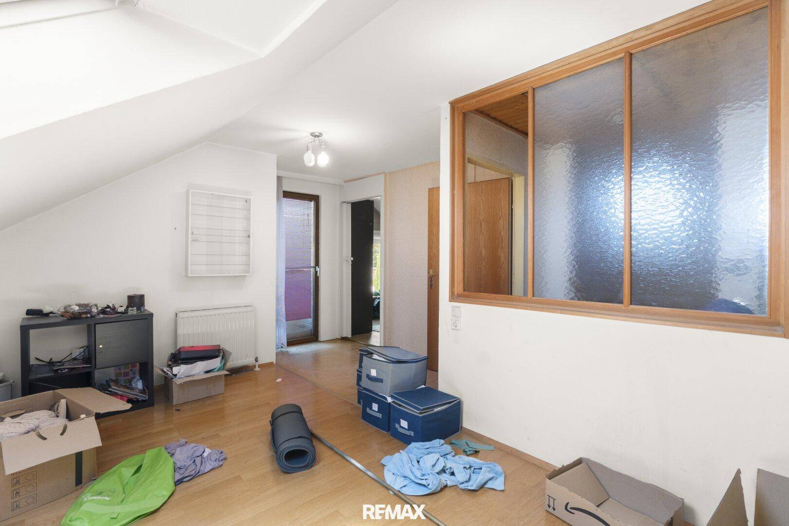 Dachgeschossraum mit schräger Decke, Holzboden und einer Tür, die ins Freie führt.